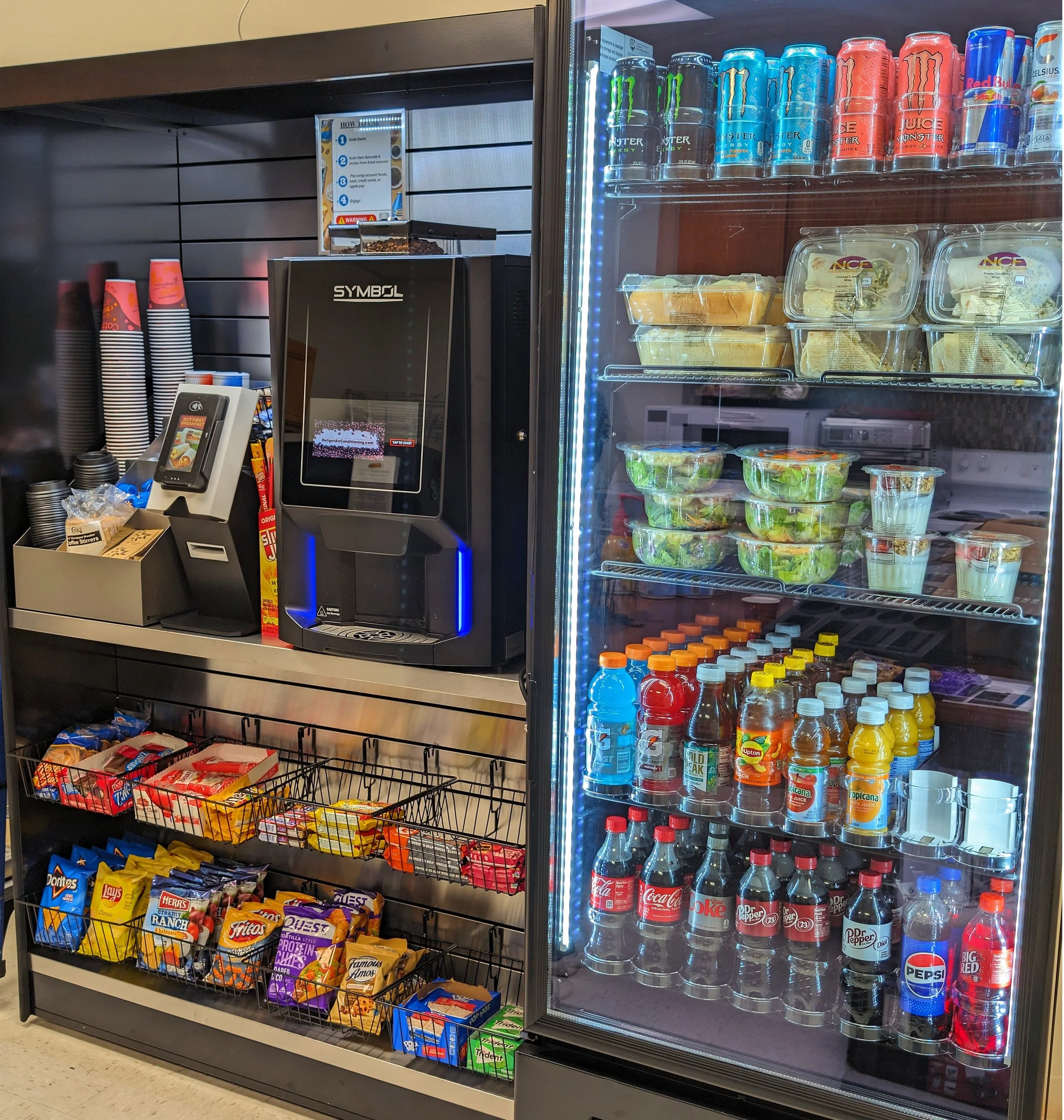Snack and beverage section of a convenience store or snack bar with chips, candy, and various sodas including Coca-Cola, Pepsi, Dr. Pepper, and Red Bull.