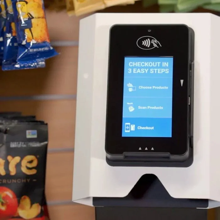 Touchscreen checkout kiosk displaying instructions for three steps: choose products, scan products, and checkout, in a retail store setting.