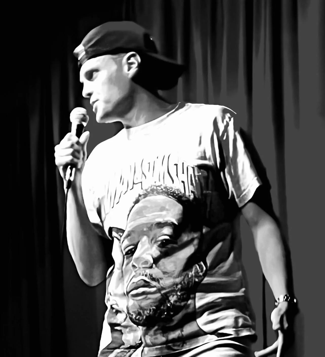 Sam Knox wearing a baseball cap and a T-shirt with a large portrait of a man's face holding a microphone on a stage with dark curtains.
