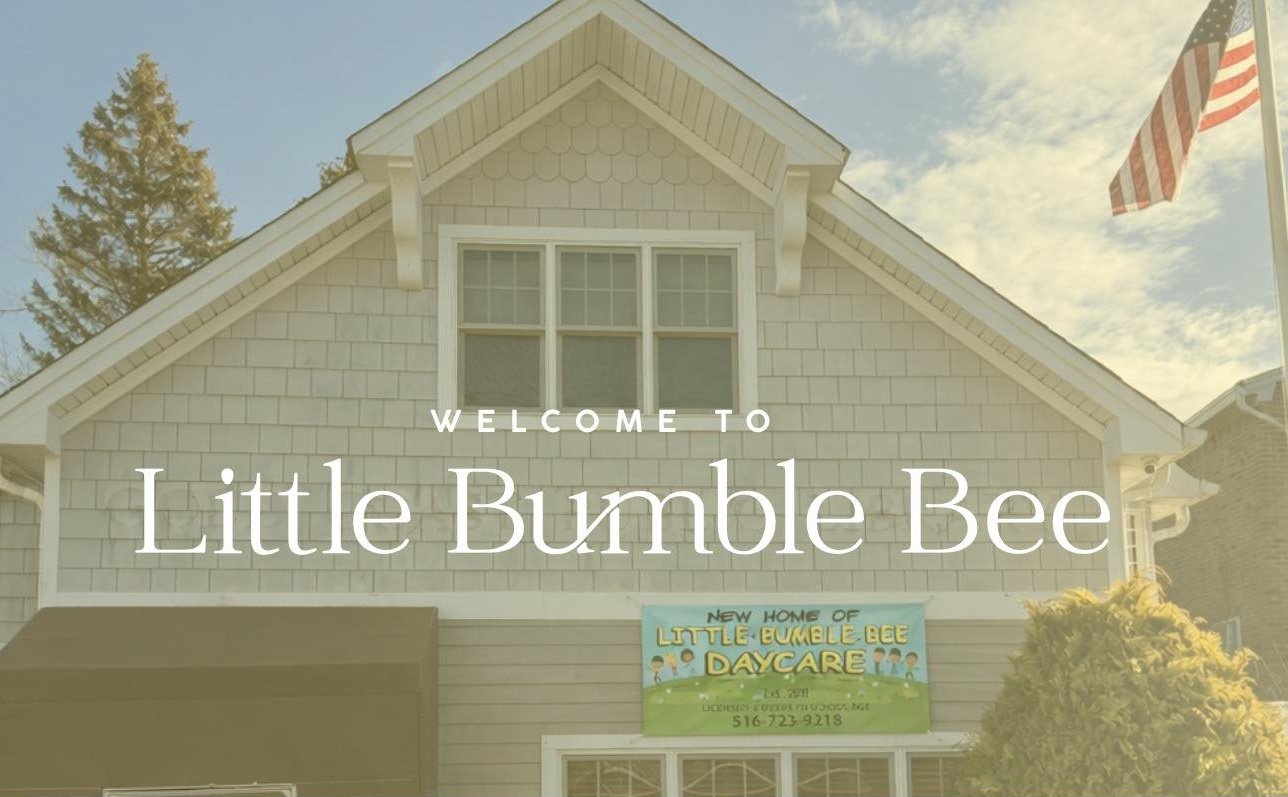 A two-story building with a sign that reads "Little Bumble Bee Daycare." An American flag is on a pole to the right. The building has beige shingles, a front window with six panes, and a covered entrance. There are trees in the background and a sky with some clouds.