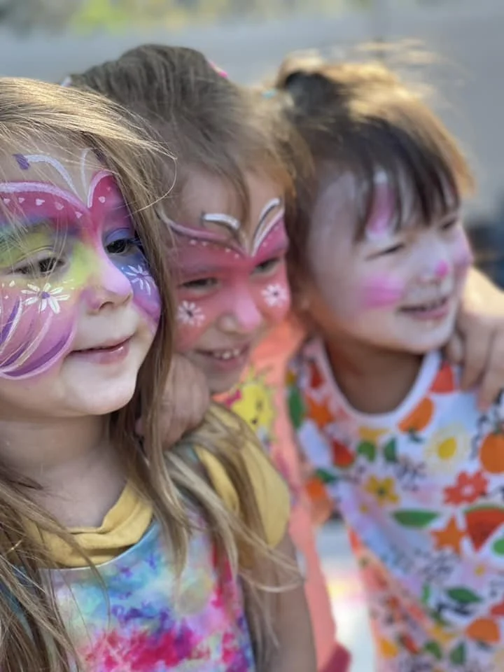 Three young girls with face paint smiling and leaning close together.