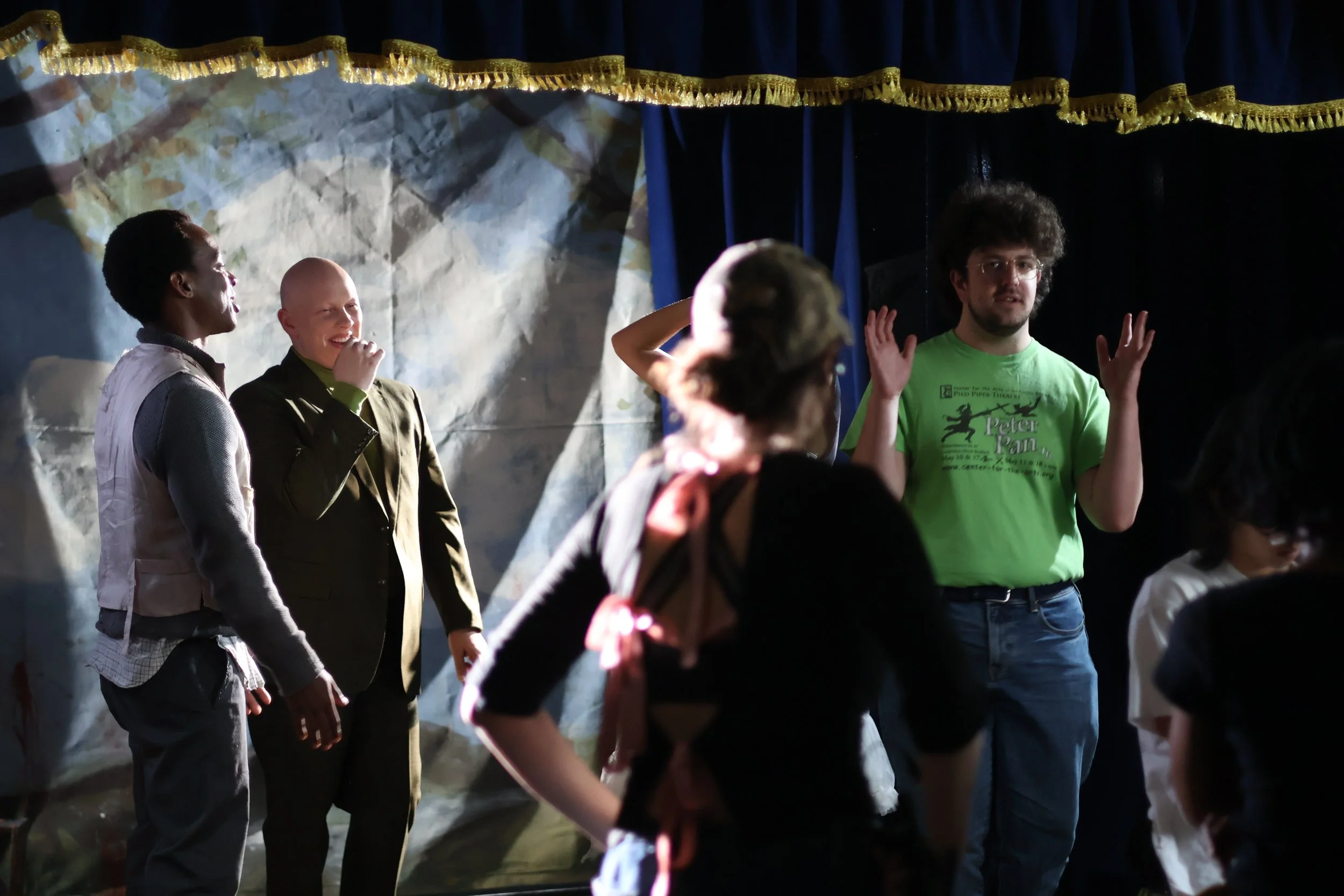 People gathered on stage during a performance or event, with a curtain and painted backdrop behind them.
