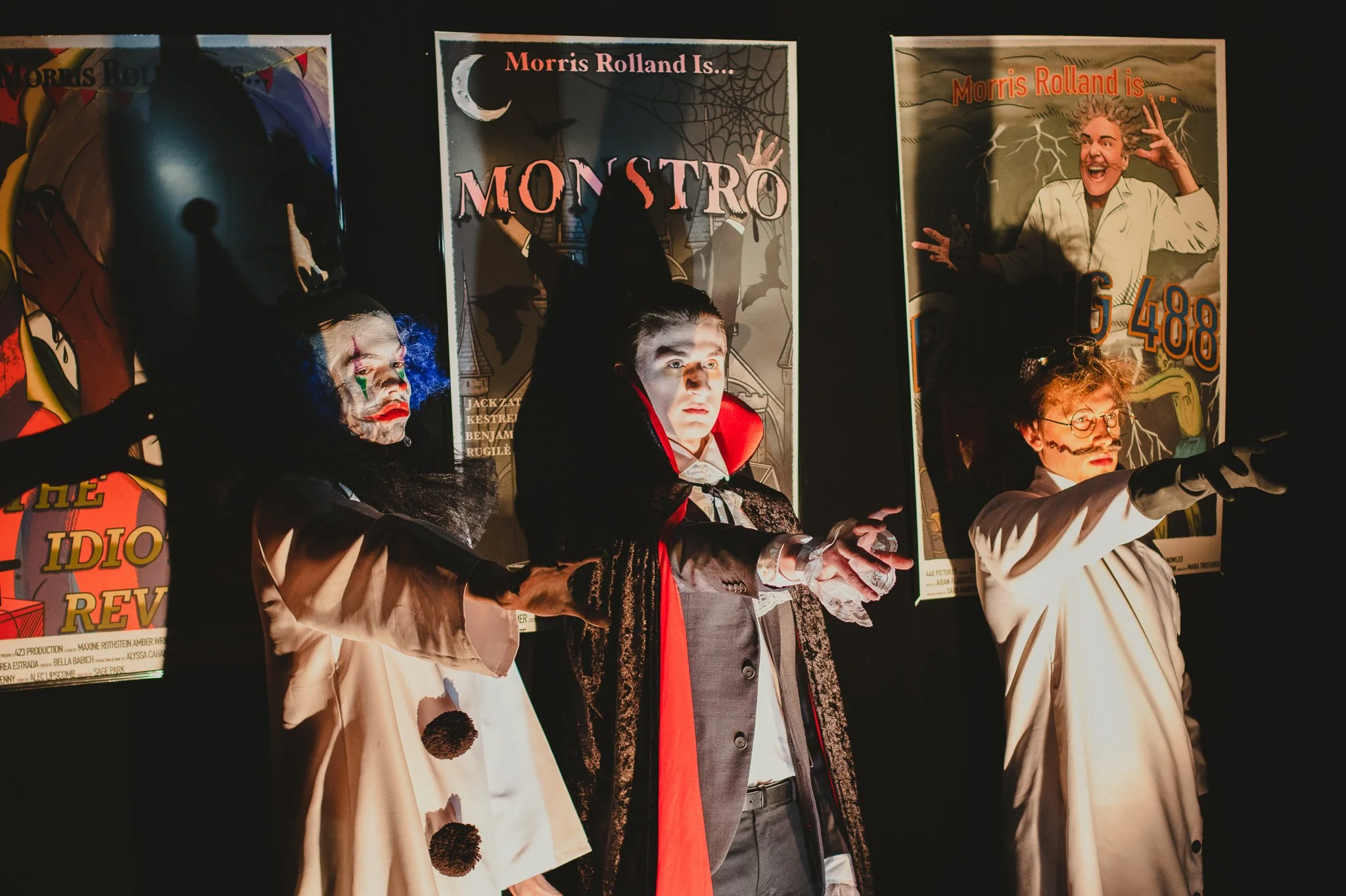 Several people dressed as horror characters from a movie, standing in front of posters of the film 'Monstro', with one person in a Dracula costume and another in a Frankenstein costume.