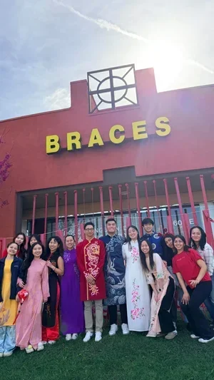 Group of people dressed in traditional Vietnamese áo dài in front of a store with a red facade and yellow sign reading 'BRACES'.