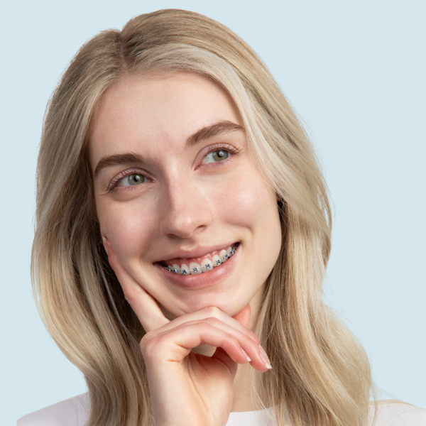 Close-up of a person's mouth with braces on their teeth, with an orthodontist using a dental tool near the braces.
