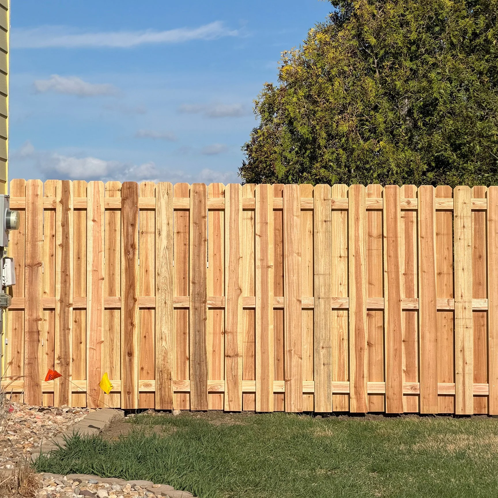 New wooden privacy fence installed in backyard with grass, rocks, and some construction flags in the foreground.
