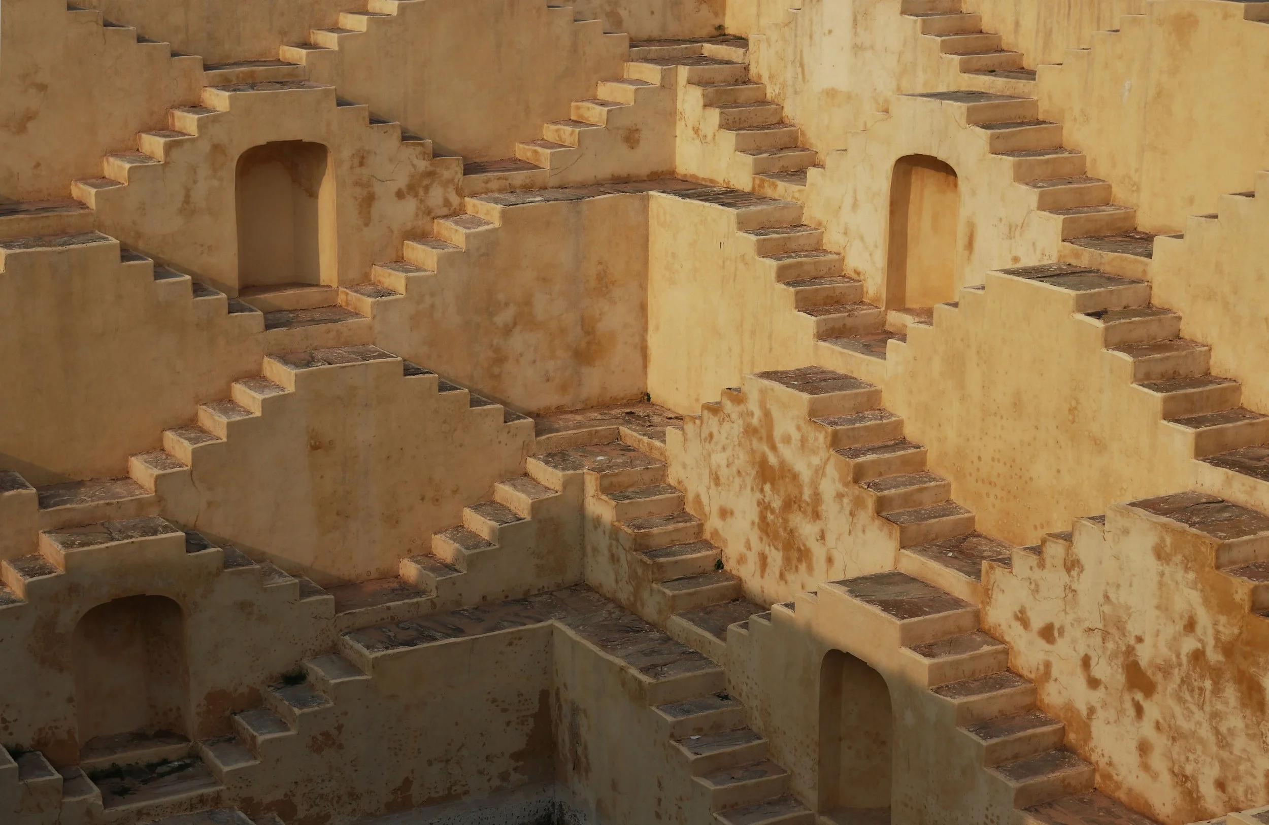 A complex stairway structure with multiple flights of stairs and small doorways, in a yellowish, weathered plaster wall.