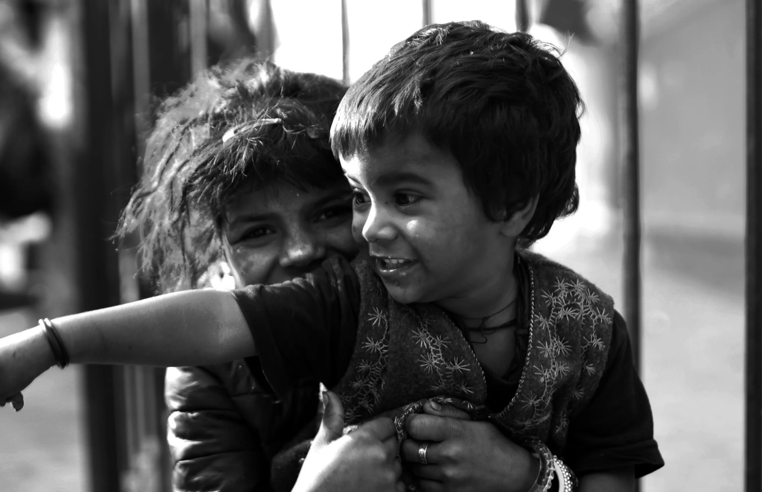 Two children, smiling and hugging each other, one with curly hair and the other with short straight hair, in a candid moment.