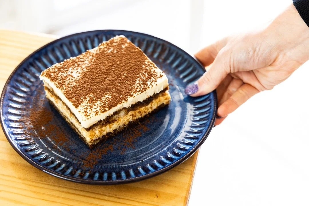 A square piece of tiramisu on a dark blue plate.