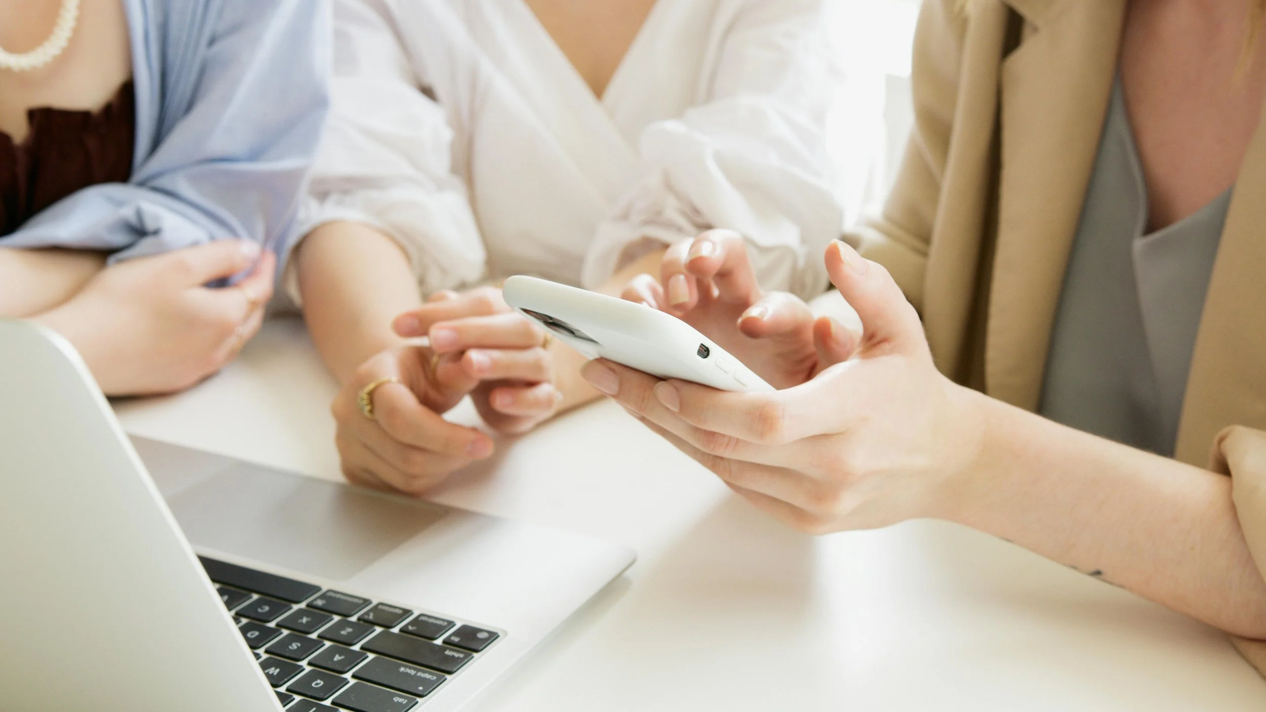 People gathered around a table looking at a smartphone, with a laptop in front of them.