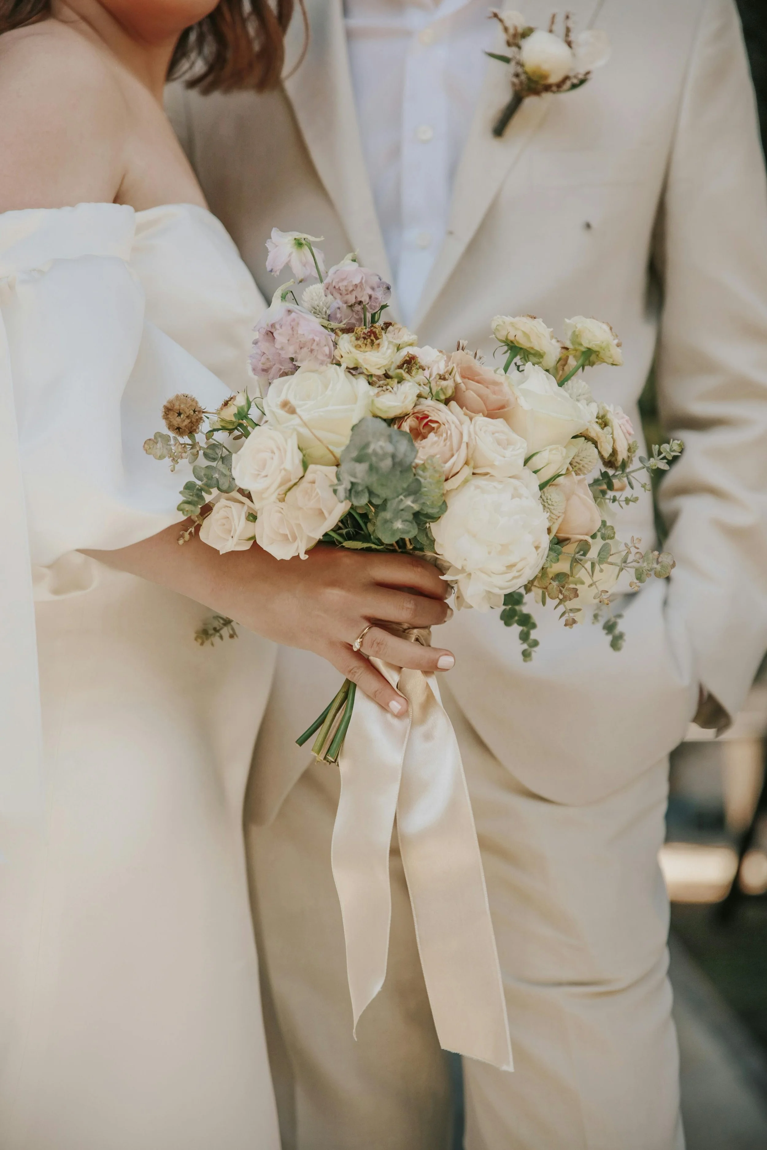 Bride holding a bouquet of white and blush roses and other flowers during a wedding ceremony.