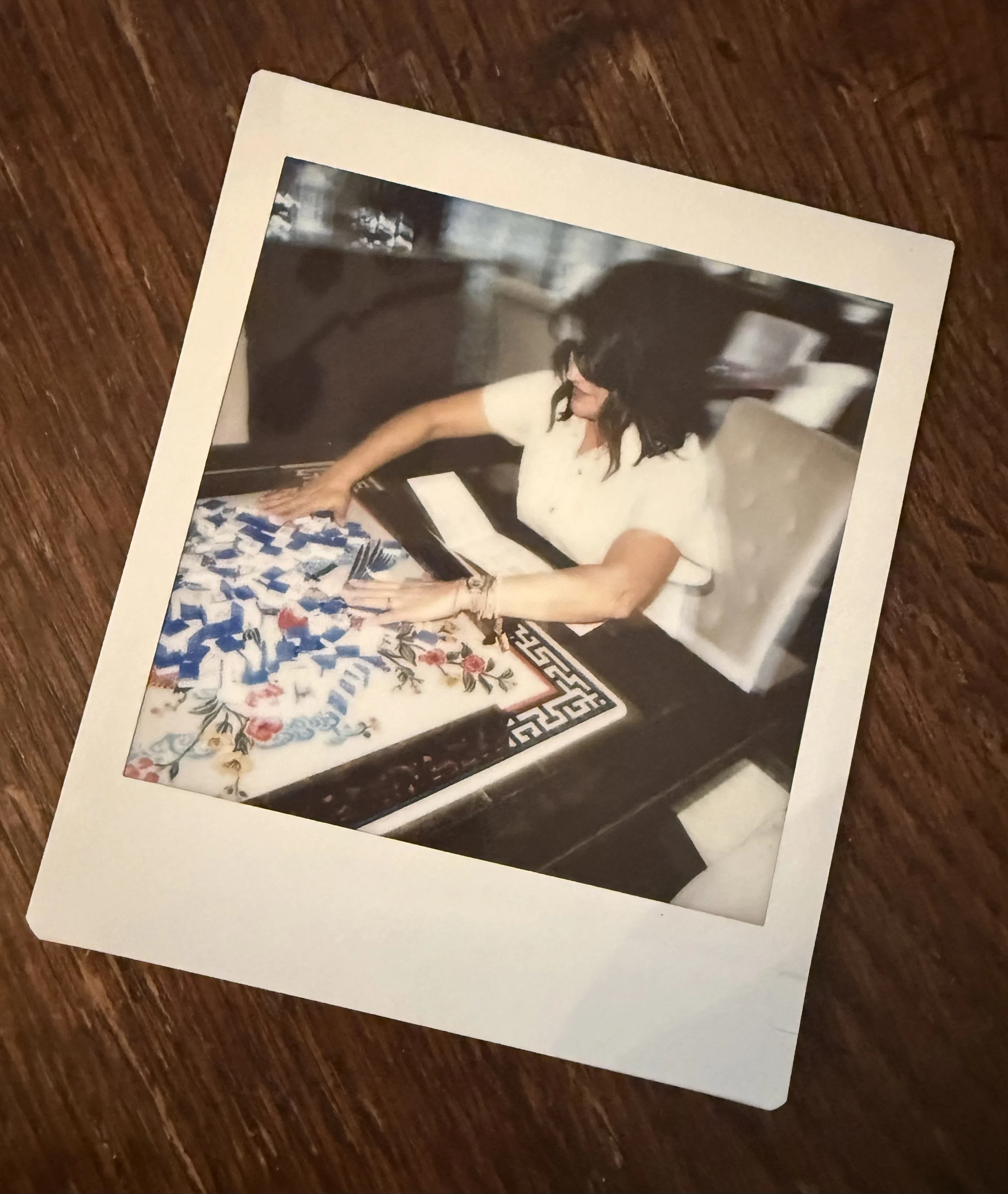 A woman with dark hair and a white shirt sitting at a mahjong table.