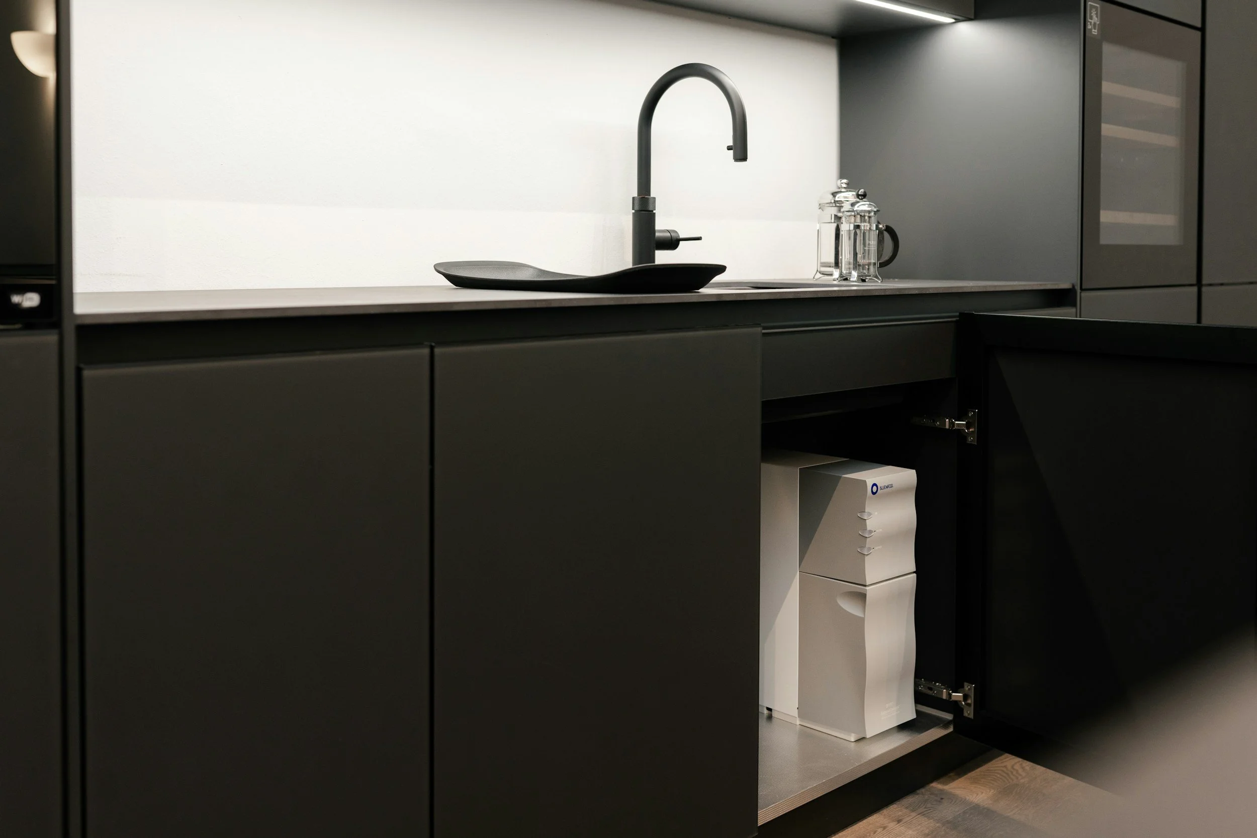 Modern kitchen with black cabinets, a black sink with a black faucet, and a white water purification system under the sink.
