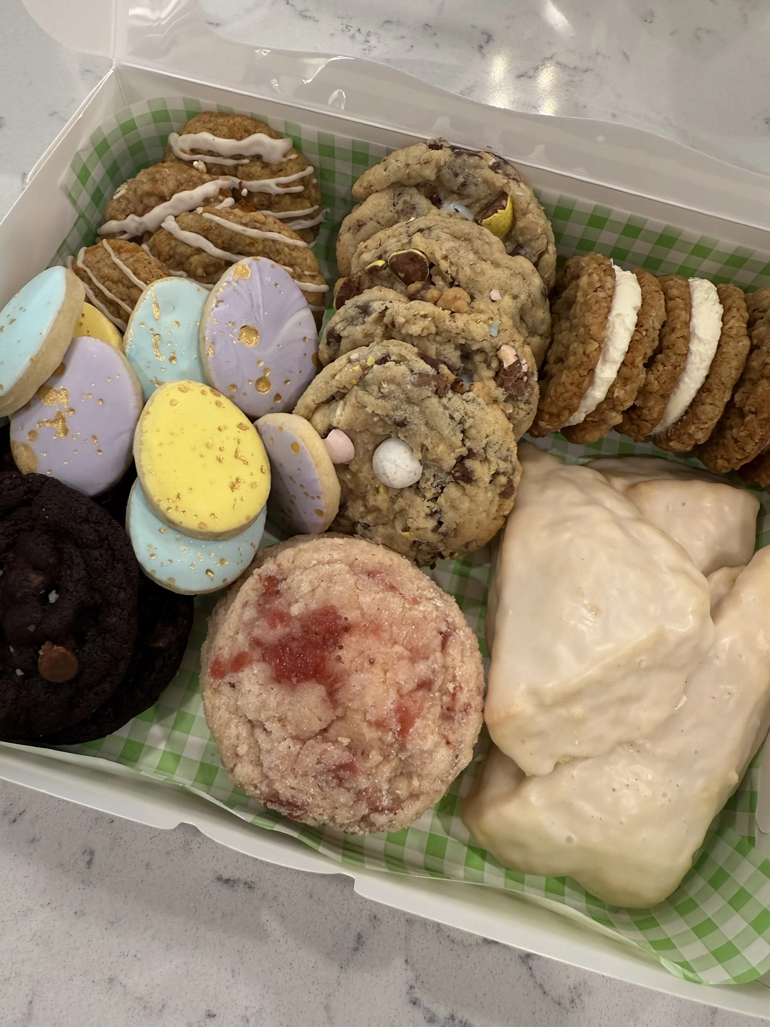 Variety of decorated cookies, chocolate chip cookies, oatmeal cookies, and frosted treats in a green checkered-lined box.