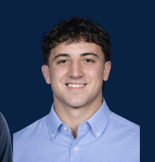 Young man with dark curly hair wearing a light blue button-up shirt, smiling, against a dark blue background.