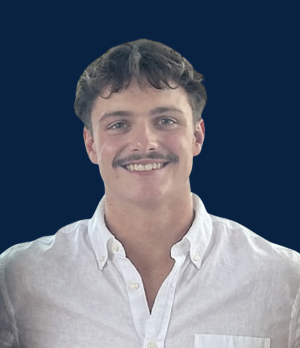 Portrait of a young man with dark hair and a mustache, wearing a white collared shirt, standing against a dark blue background.