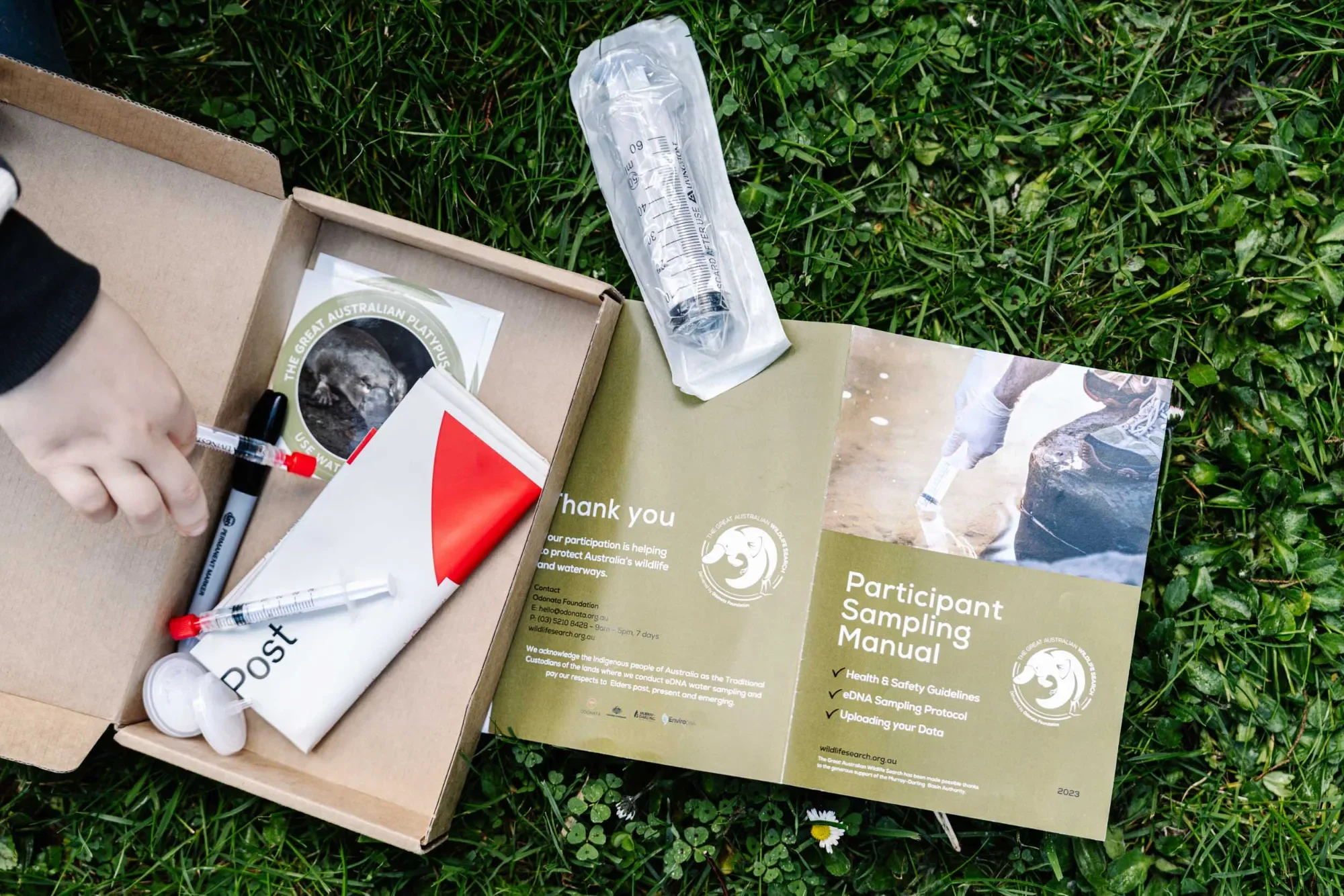Opened eDNA sampling kit on grass with swabs, a syringe and a participant manual for the Great Australian Wildlife Search.