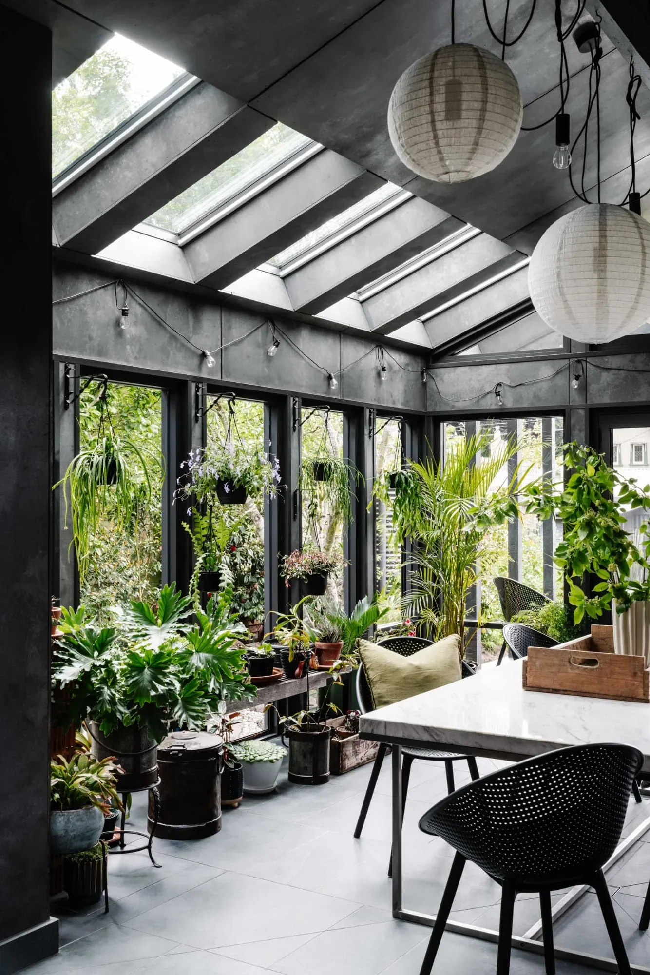 Greenhouse Grove, a dark-framed sunroom filled with potted plants and skylights, showing biophilic design.
