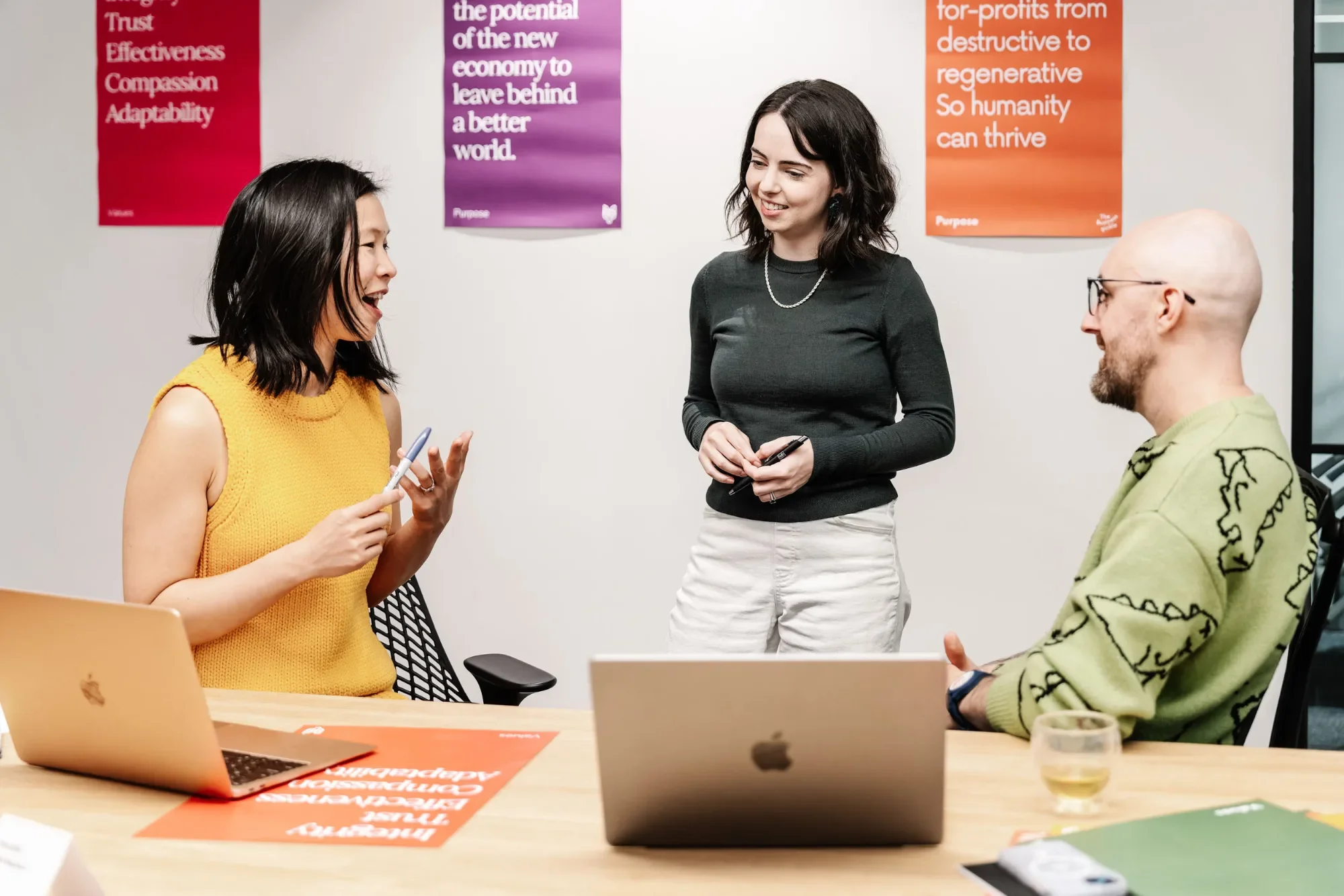 Three people talking around a desk with laptops at Harvey, a marketing agency