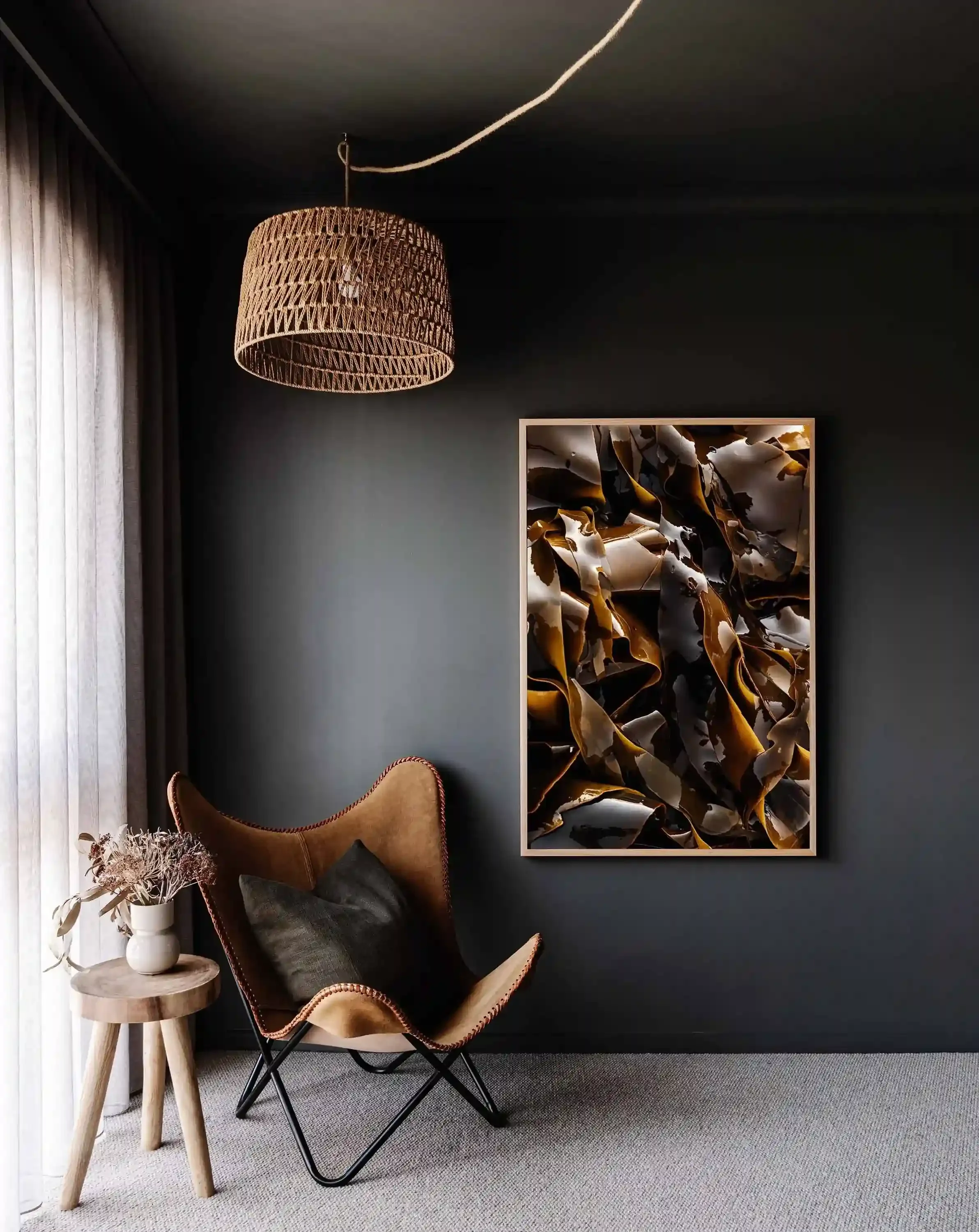 Framed abstract photograph of glossy brown kelp displayed on a dark gray wall beside a tan leather chair.