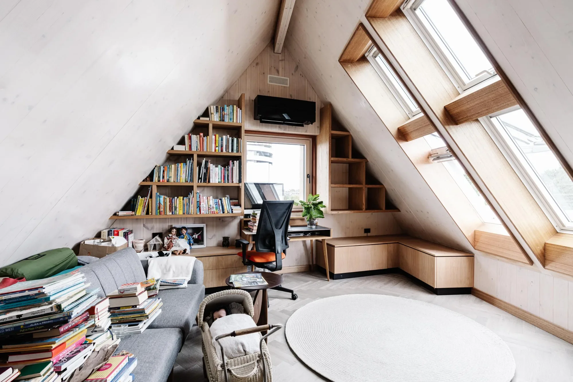 Hutt Haus attic living space before decluttering, with piles of books, a cluttered sofa and busy shelves.