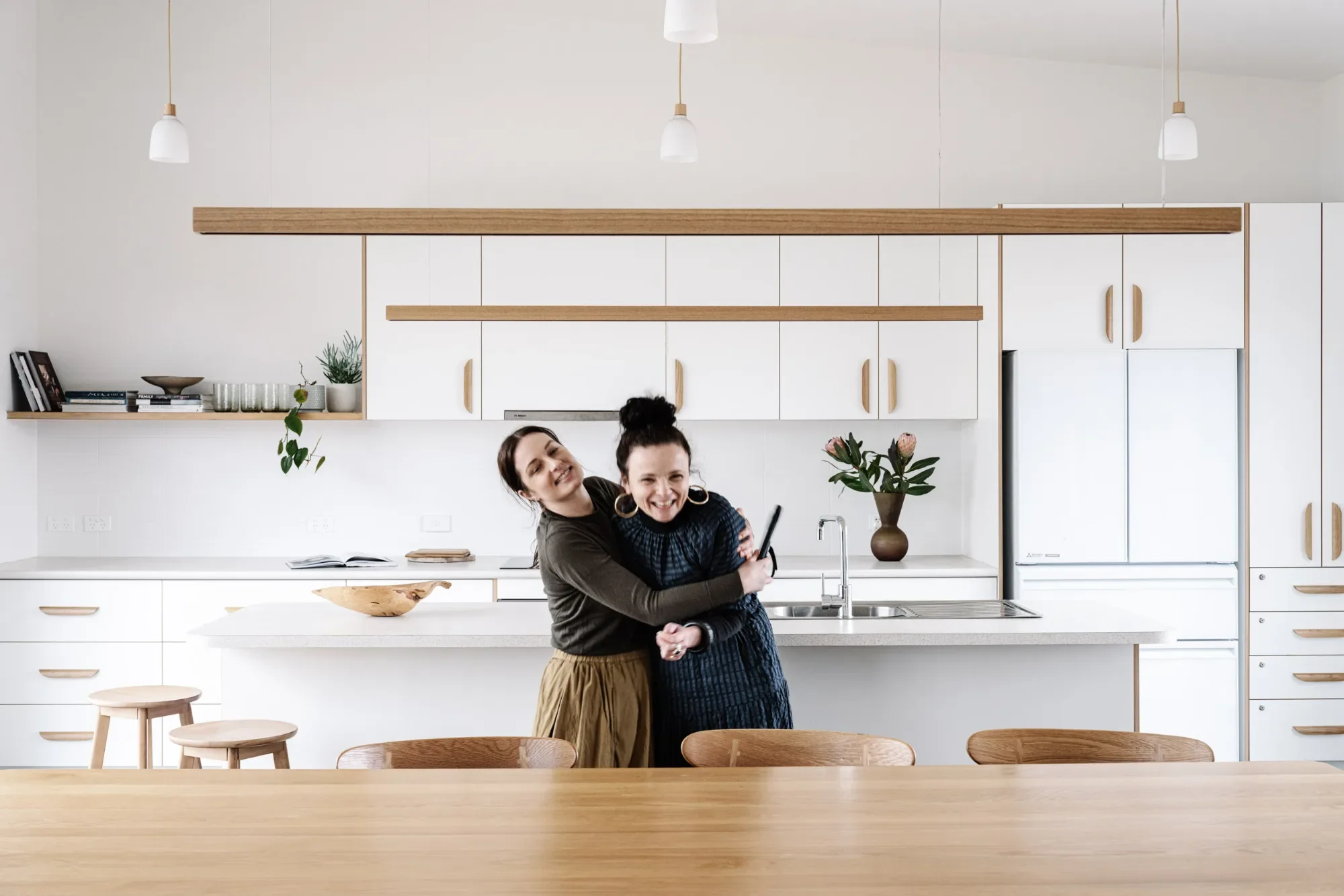 Marnie Hawson and stylist Belle sharing a hug in a bright kitchen before a styled shoot.