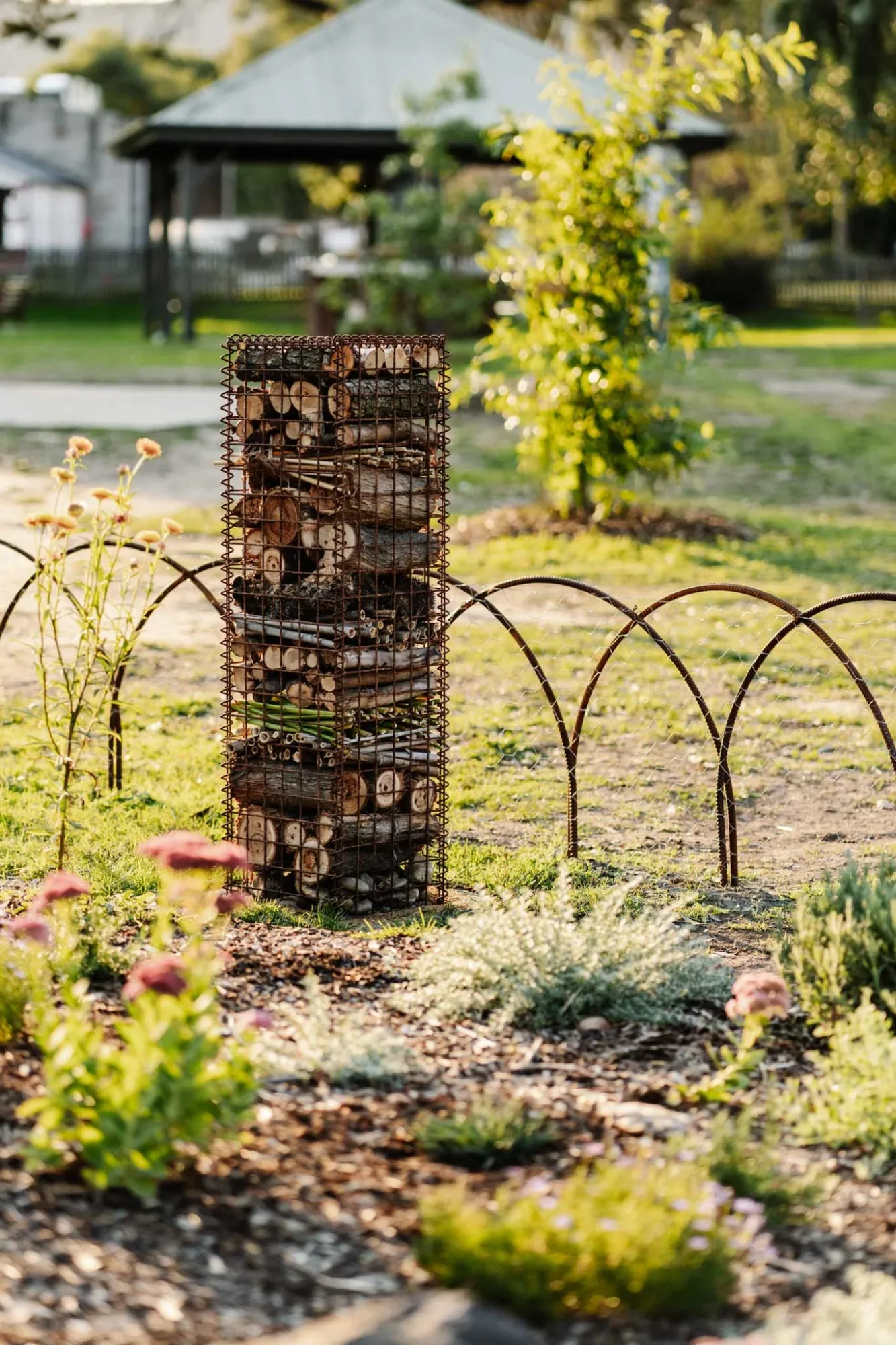A wire-and-log insect hotel standing in a native garden bed, offering shelter for insects.