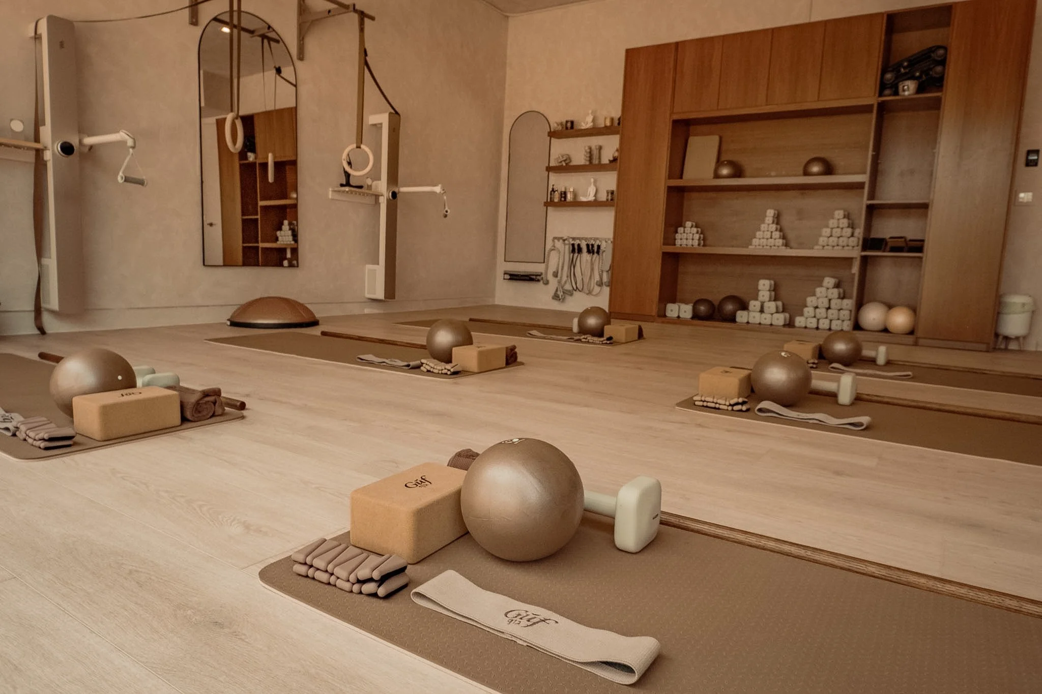 Yoga mats, blocks, and exercise balls set up in a yoga or fitness studio with shelves and mirrors in the background.