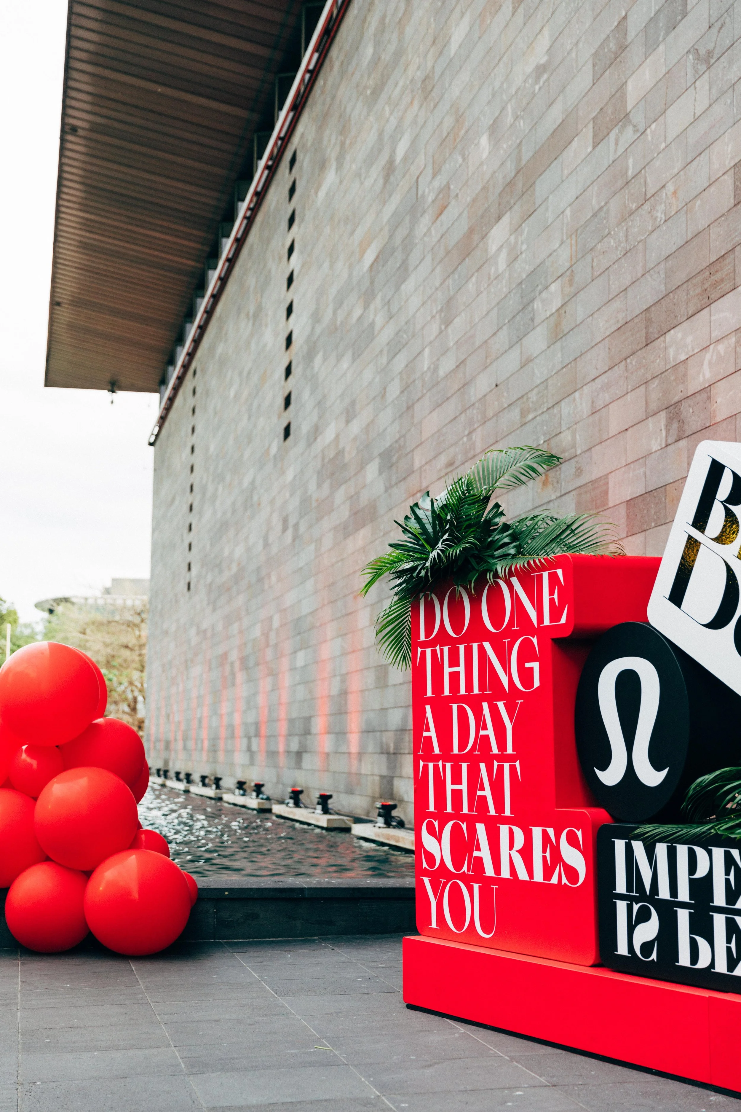 Red balloons on the left, colorful display with motivational quotes on the right, against a brick wall background.