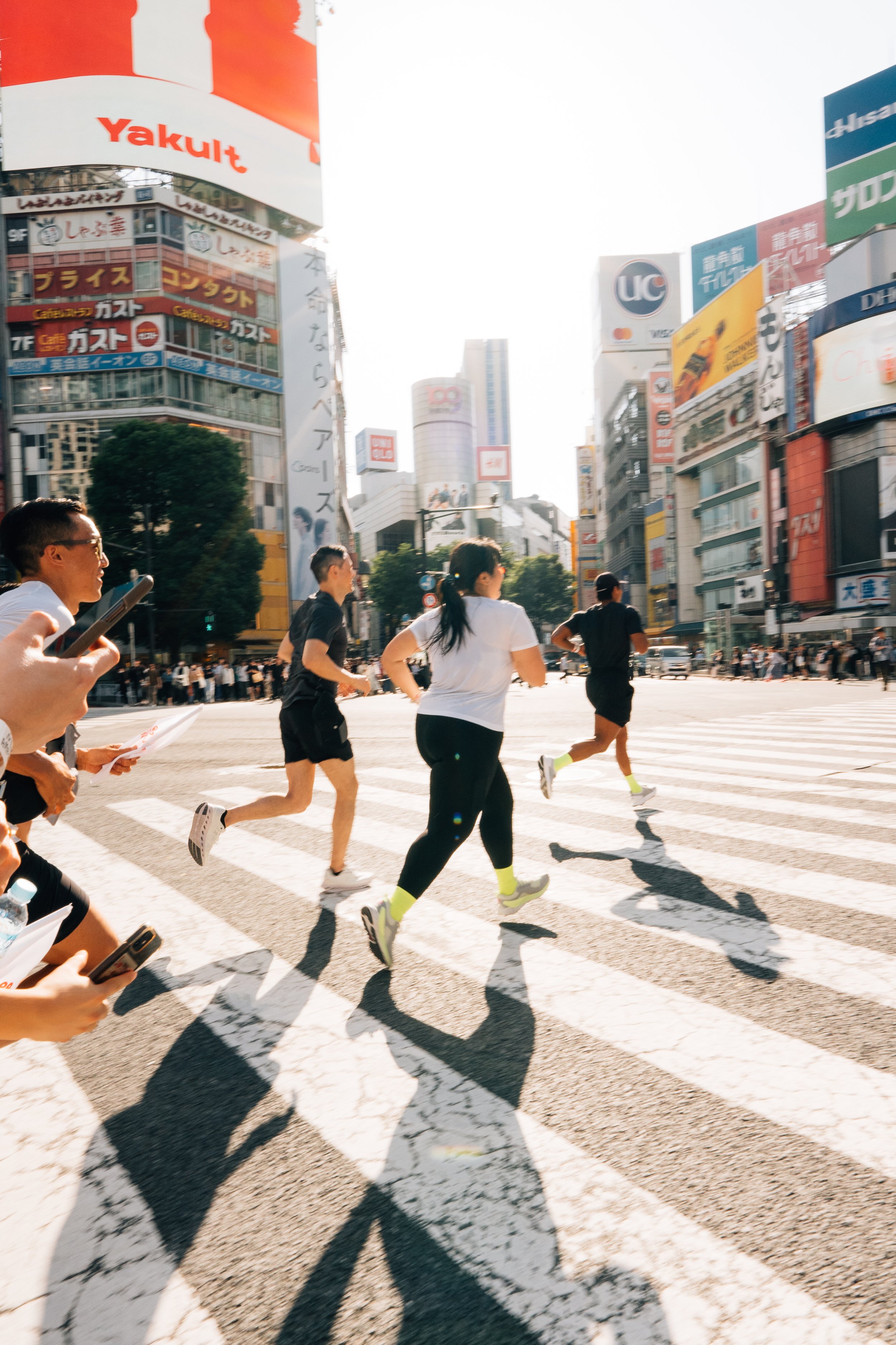 People running across a busy city street in Tokyo with tall buildings and billboards in the background.