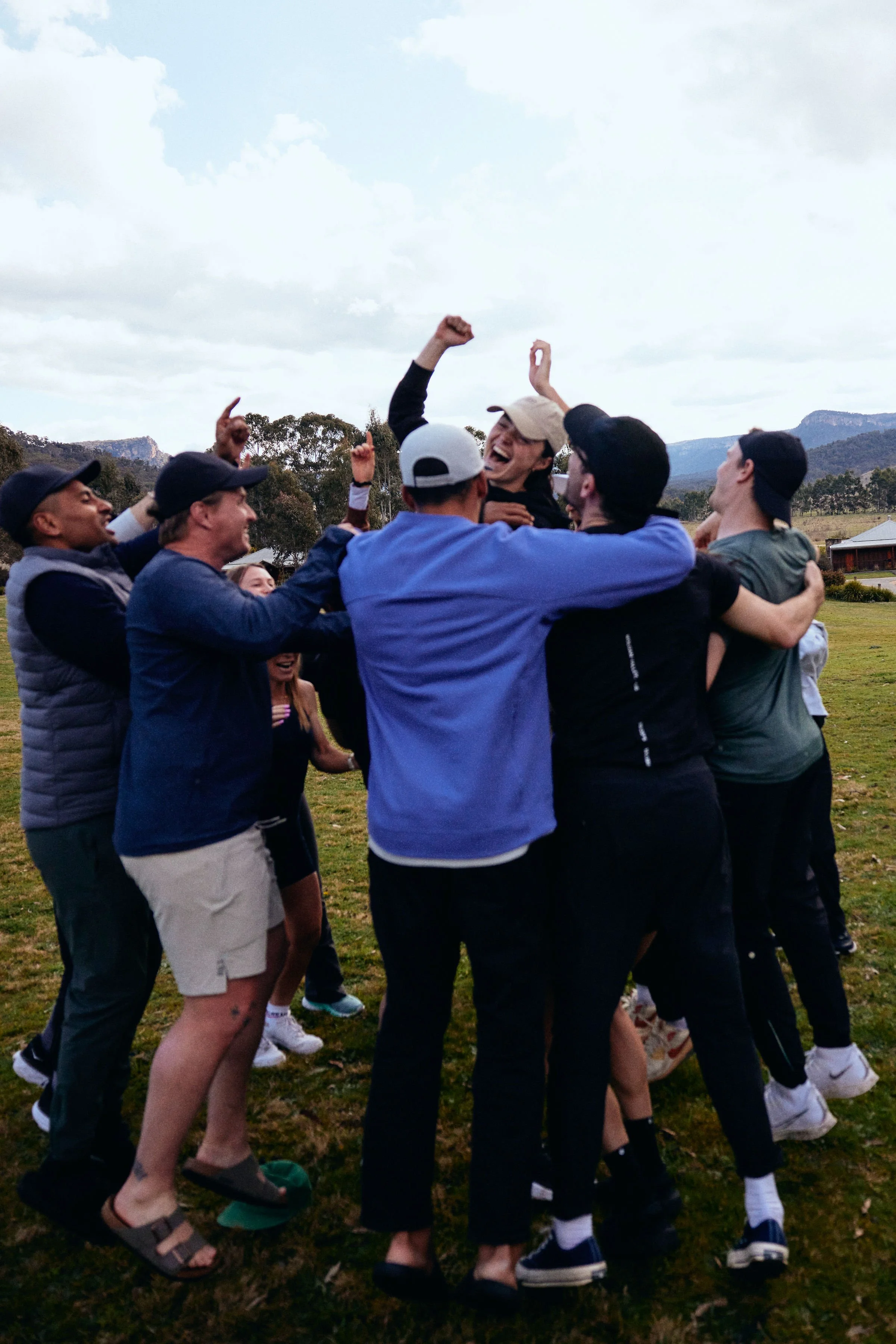 A group of people outside in a grassy field with mountains in the background, celebrating and hugging each other.