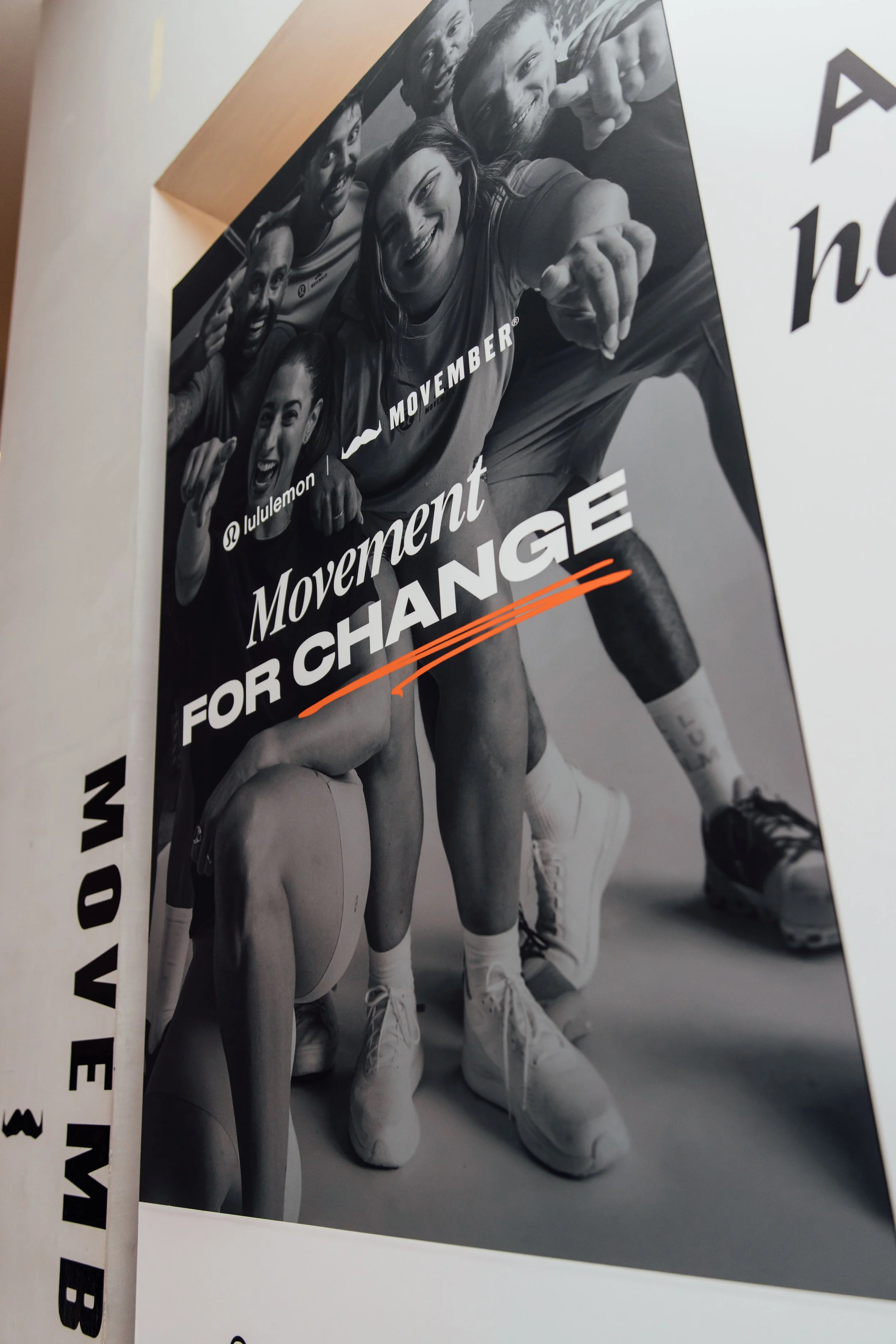 Black and white photograph of a group of young people in athletic attire, smiling and posing with some pointing and making hand gestures. The photo appears to be related to a movement or campaign for change for Movember