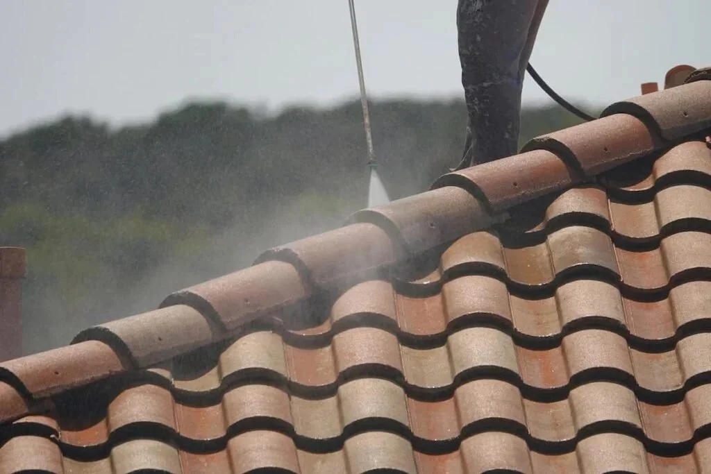 Worker pressure washing a tiled roof.