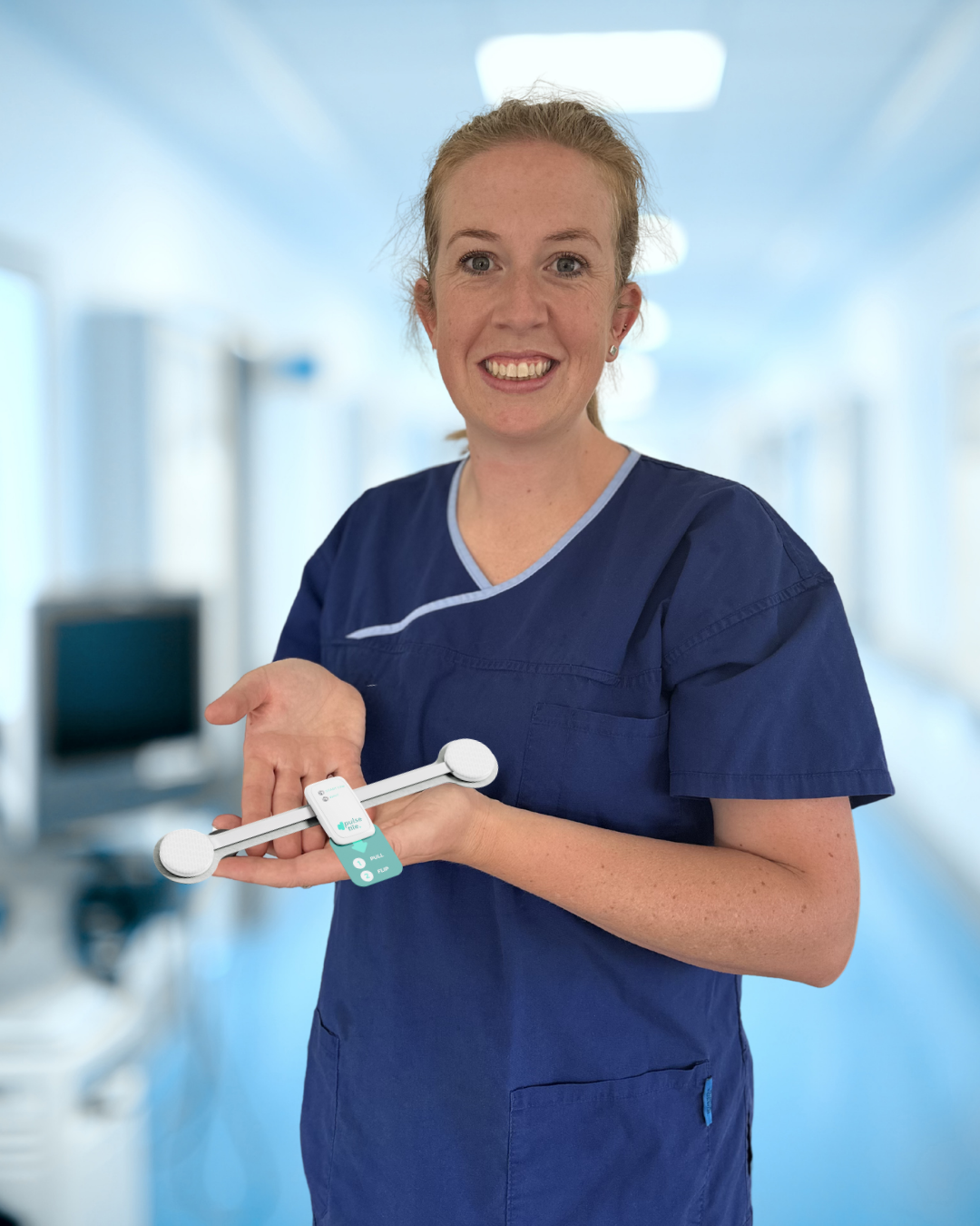 Elleesha King - Female healthcare worker in a hospital corridor holding a mindfulness or stress relief device and smiling.
