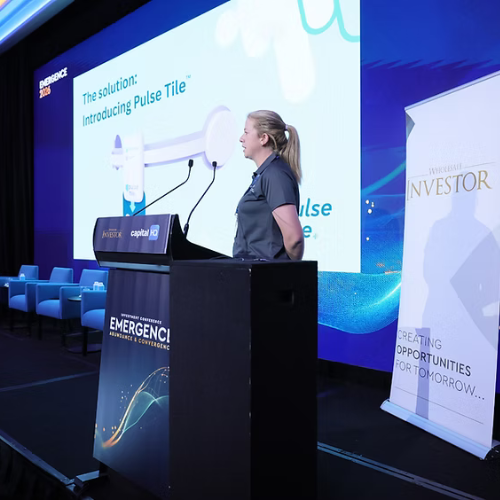 A woman presenting at a conference with a large screen behind her displaying a slide titled "The solution: Introducing Pulse Tile."