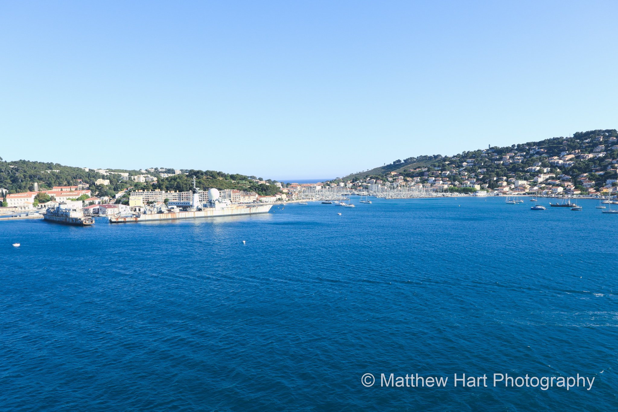 Fine art photograph of a deep blue bay on the Italian Riviera with hillside towns along the far shore under a clear summer sky.