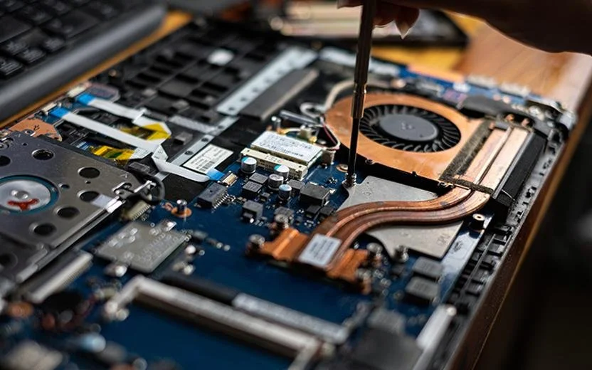 Open laptop with visible internal components like cooling fan, heat pipes, and circuit board, with a screwdriver being used to adjust or repair it.