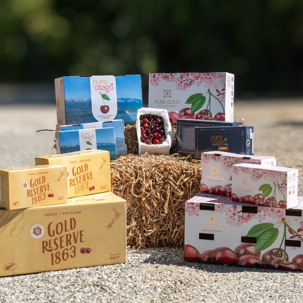Boxes of cherries and cherry products displayed on a hay bale outdoors.