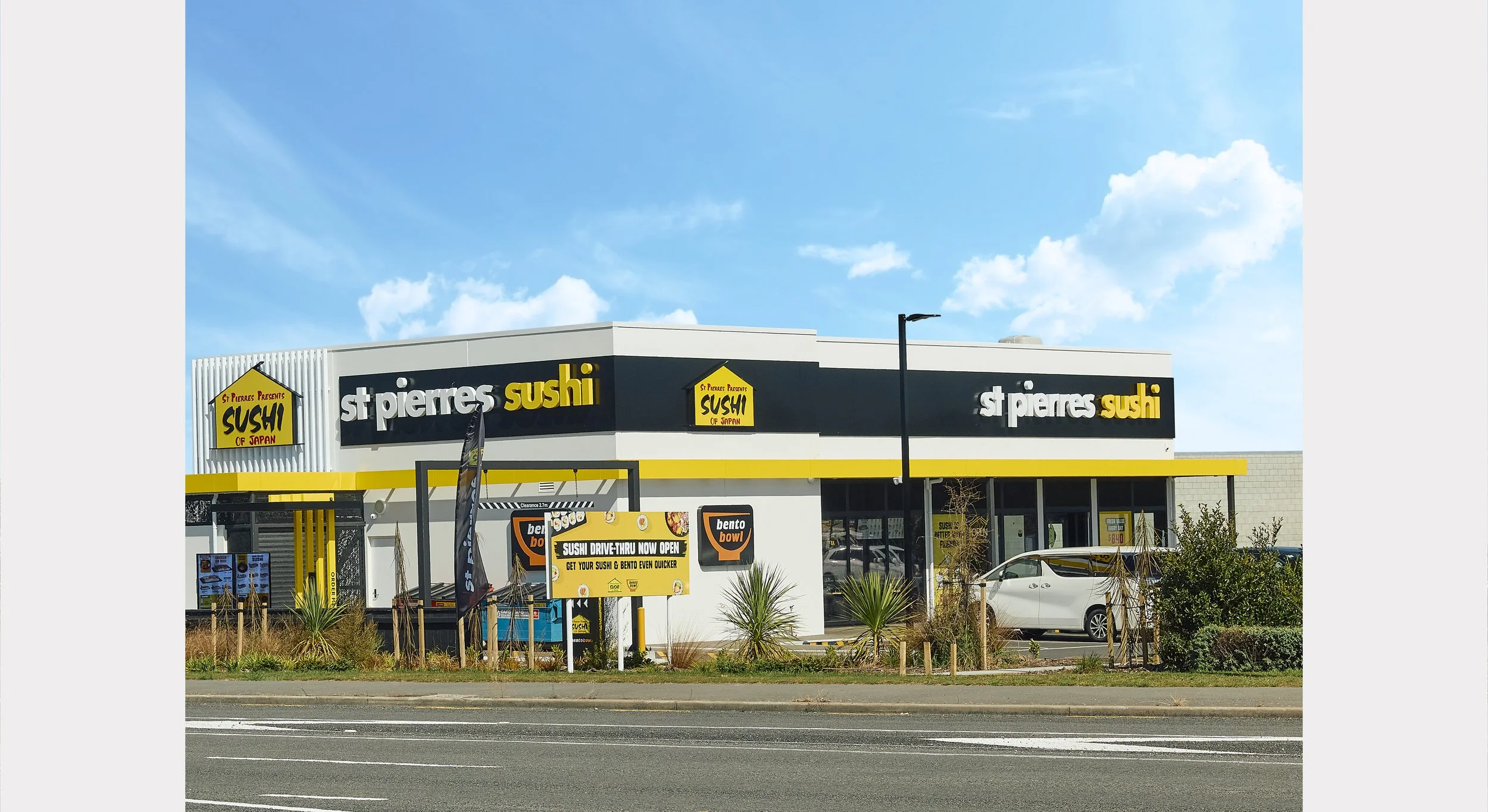 Exterior view of a sushi restaurant named "St PIERRES Sushi" with signage indicating drive-thru service and a blue sky with some clouds.