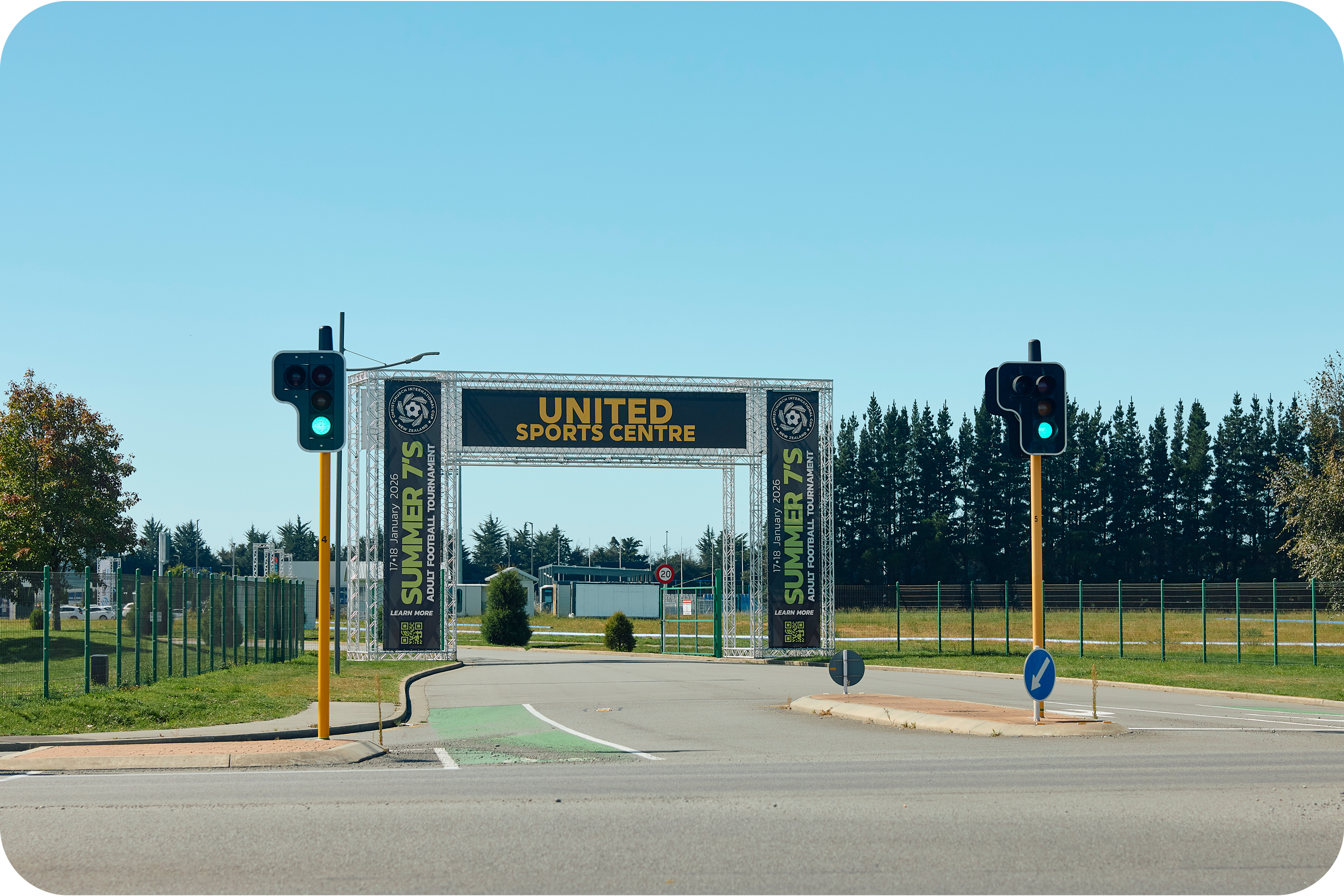A sports event entrance with two traffic lights showing green, a large banner reading 'United Sports Centre,' and trees in the background.