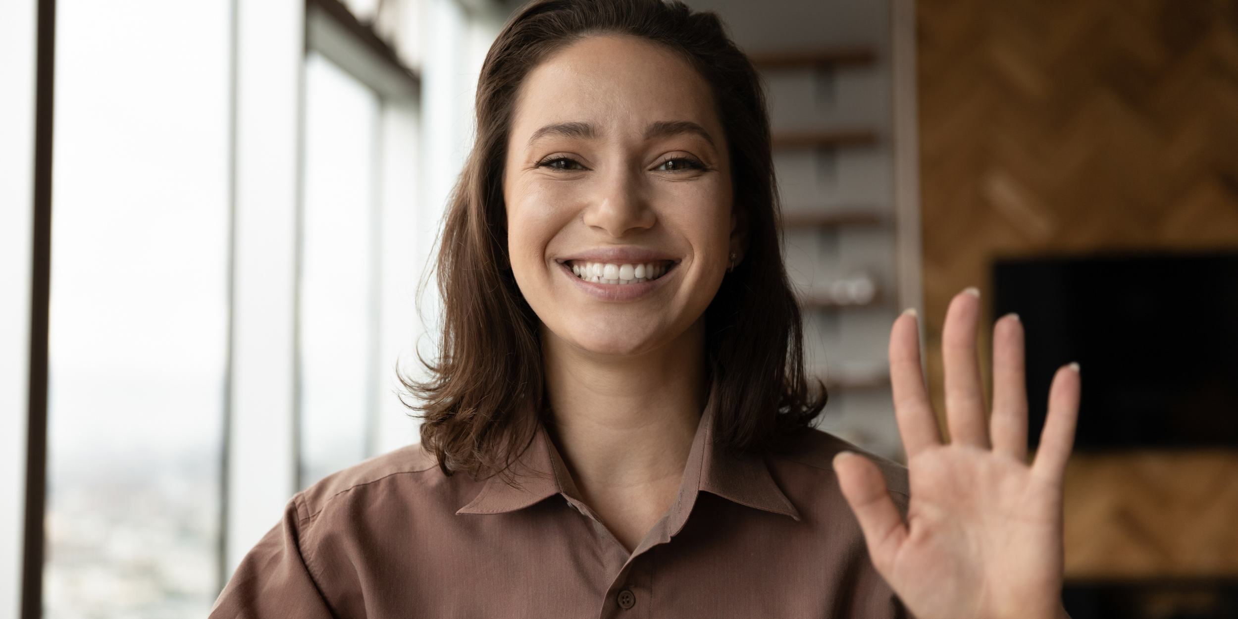 Woman wearing a brown shirt and waving to the camera