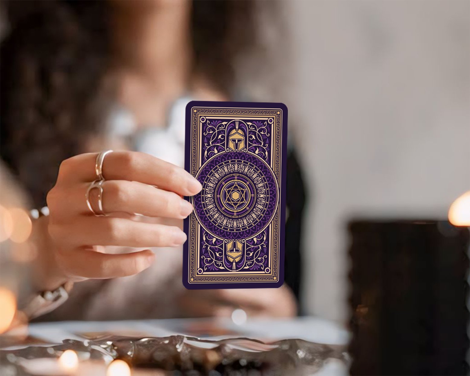 Person holding a tarot card with intricate gold and purple design, featuring sacred symbols and geometric patterns.