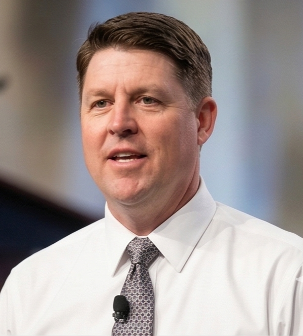 Man in white shirt and patterned tie speaking or making a point.