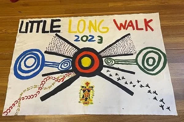 Colorful handmade poster with the text 'LITTLE LONG WALK 2023', featuring a central target-like symbol with black, yellow, and red rings, and various decorative patterns and drawing of birds and footprints.