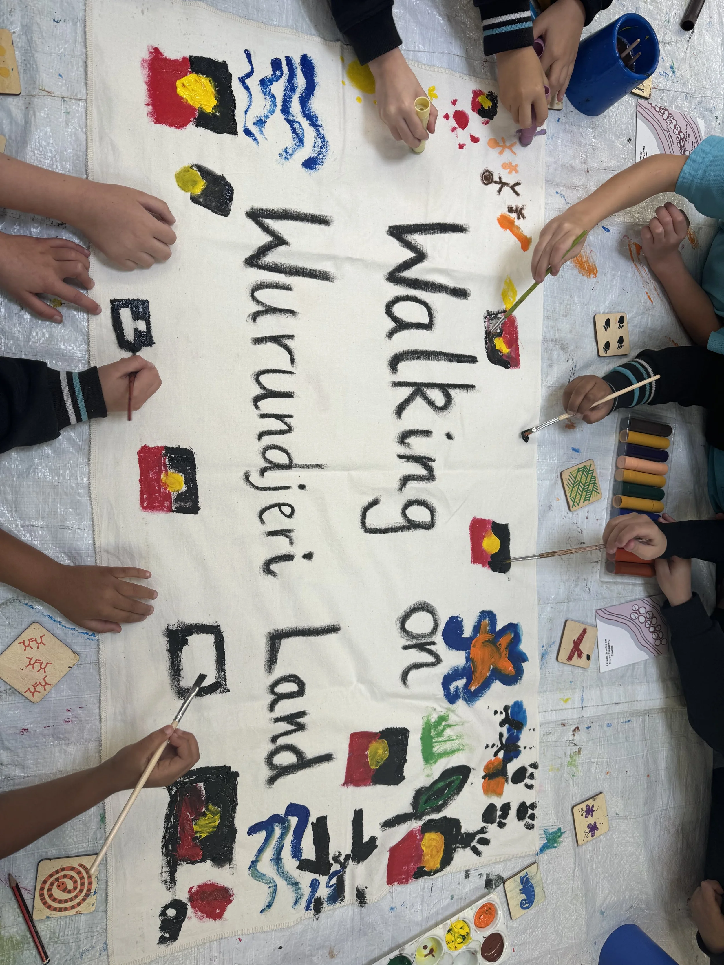 Children painting and decorating a banner with the words 'Thank you' and various colorful images and patterns.