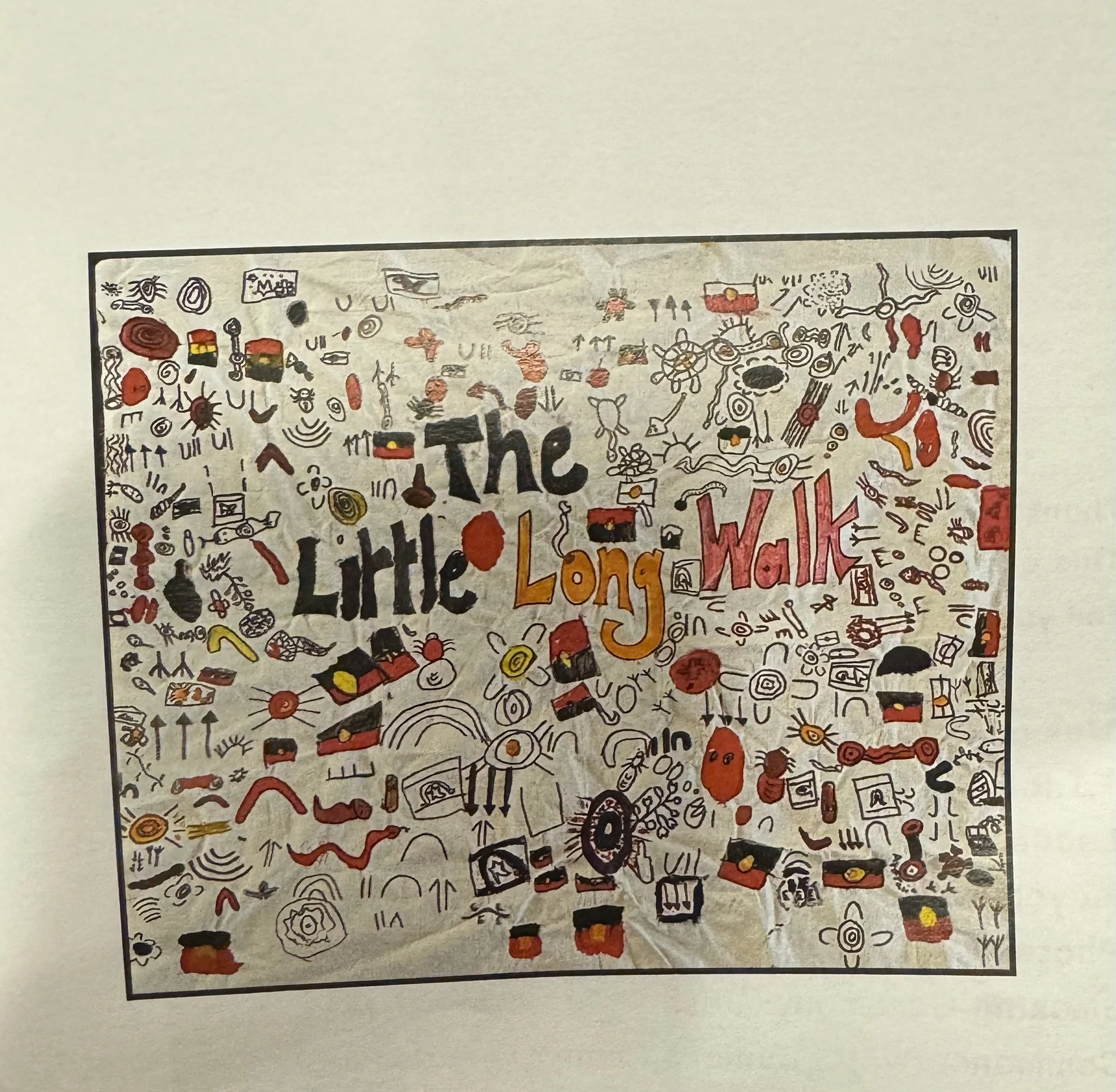 A hand-drawn poster with various small doodles and symbols in black, red, yellow, and orange, surrounding the large word "The" in the center. The poster is framed with a black border and is mounted on a white wall.