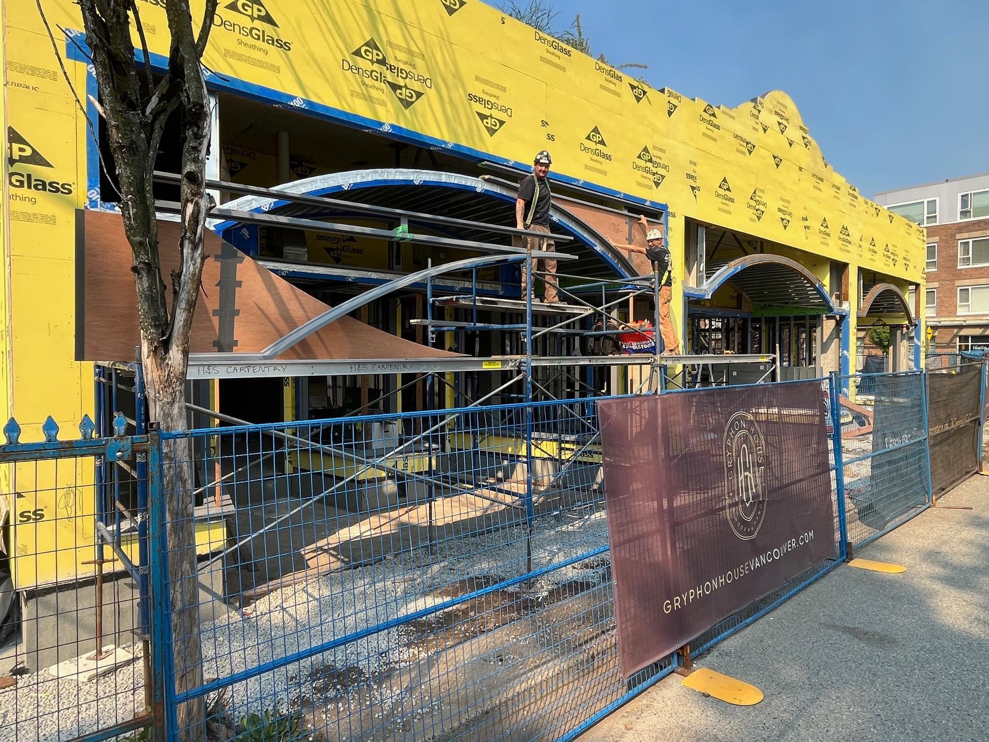 Construction site with building under construction, workers in safety gear, and a safety fence with advertisements.