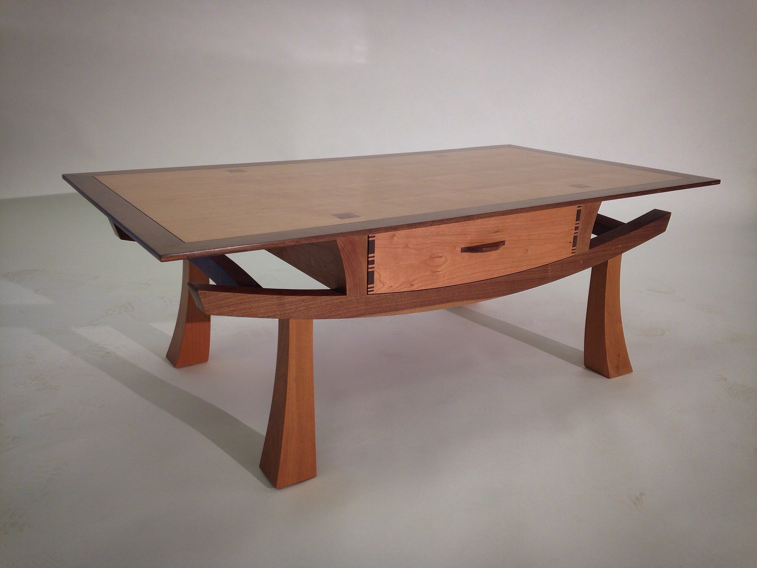 A wooden table with a curved design and an open drawer, supported by four angled legs.
