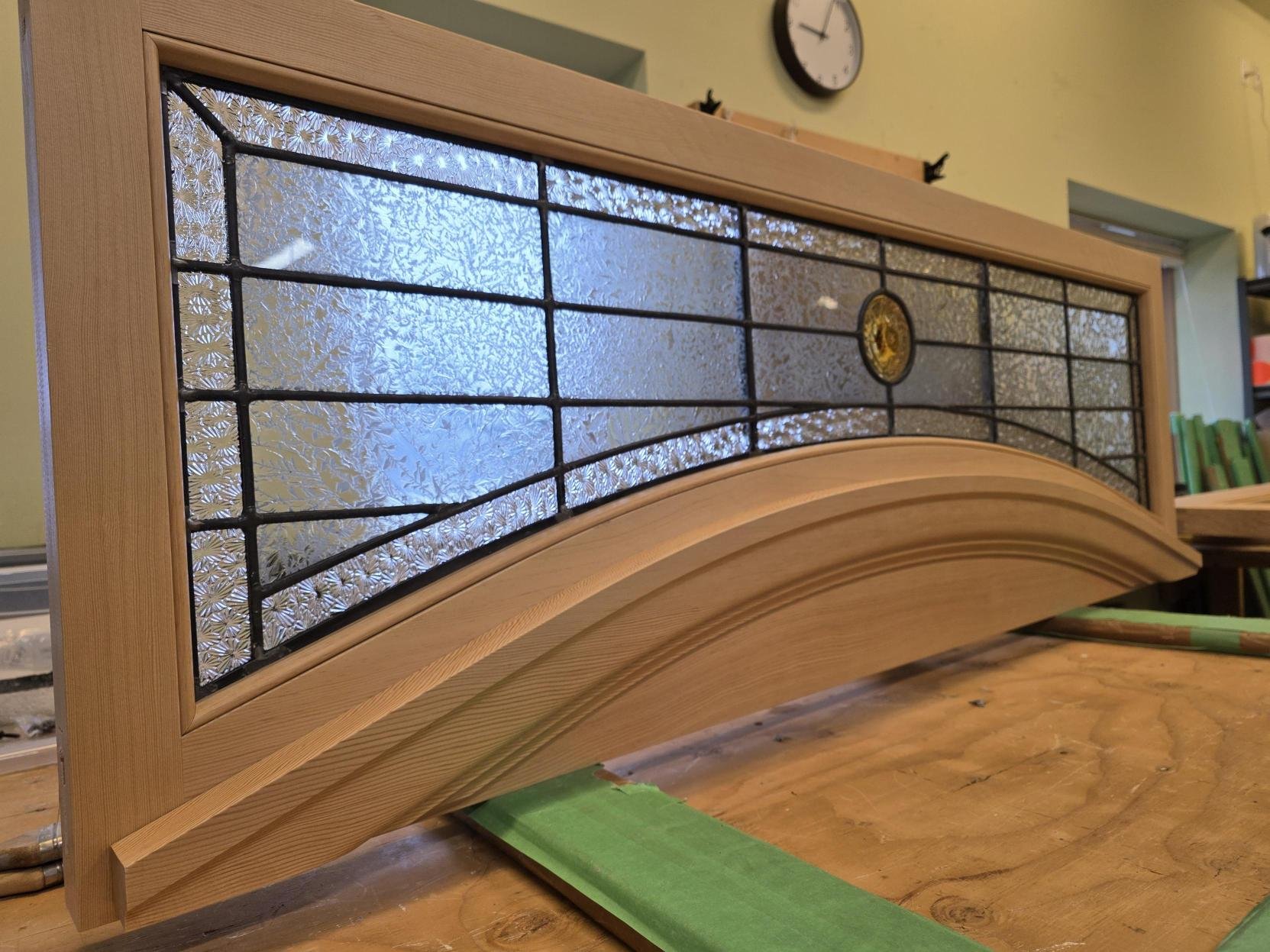 A stained glass window with a wooden frame, placed on a workbench in a craftsman's workshop.