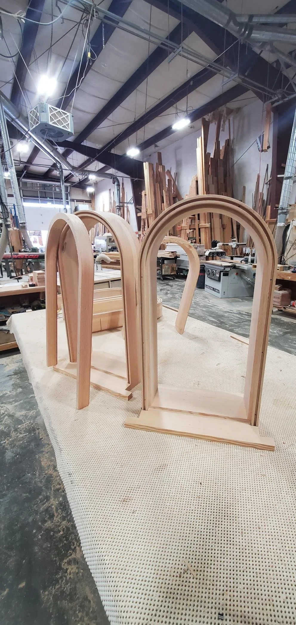 Wooden arch frames under construction in a woodworking workshop with various wooden pieces and machinery in the background.